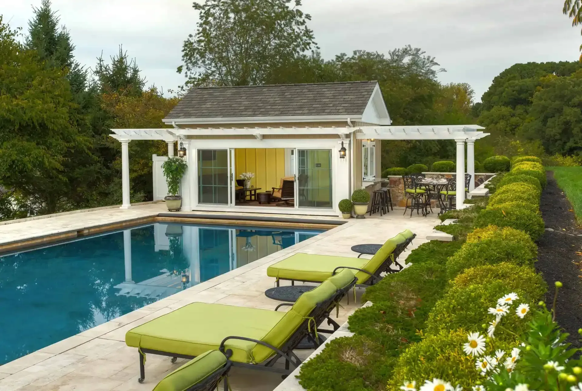 Modern backyard pool with lounge chairs beside a white house and lush garden.