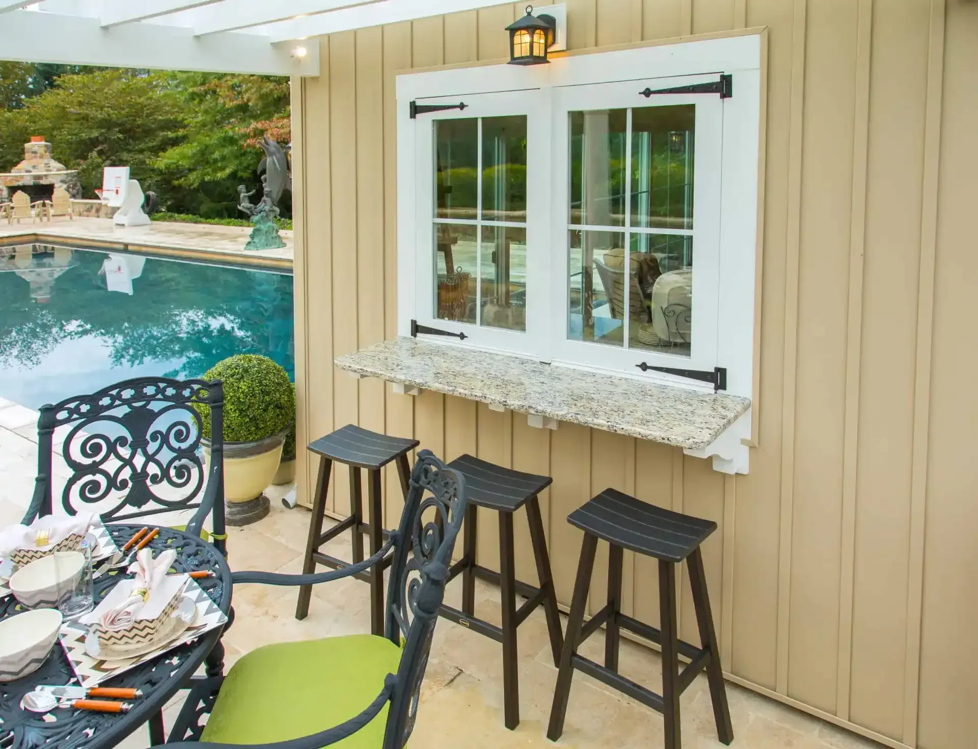 Poolside patio with stools and a serving window beside a turquoise swimming pool