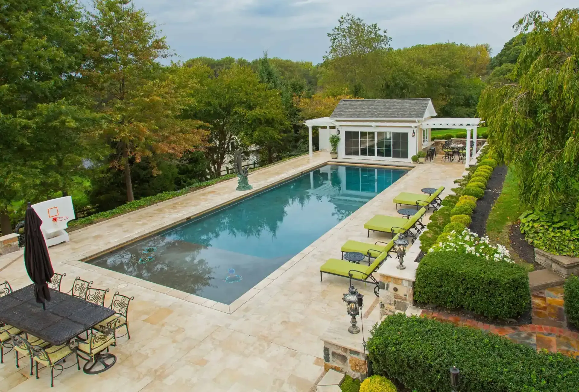 Luxury backyard pool with stone patio, lounge chairs, and a pavilion surrounded by lush greenery