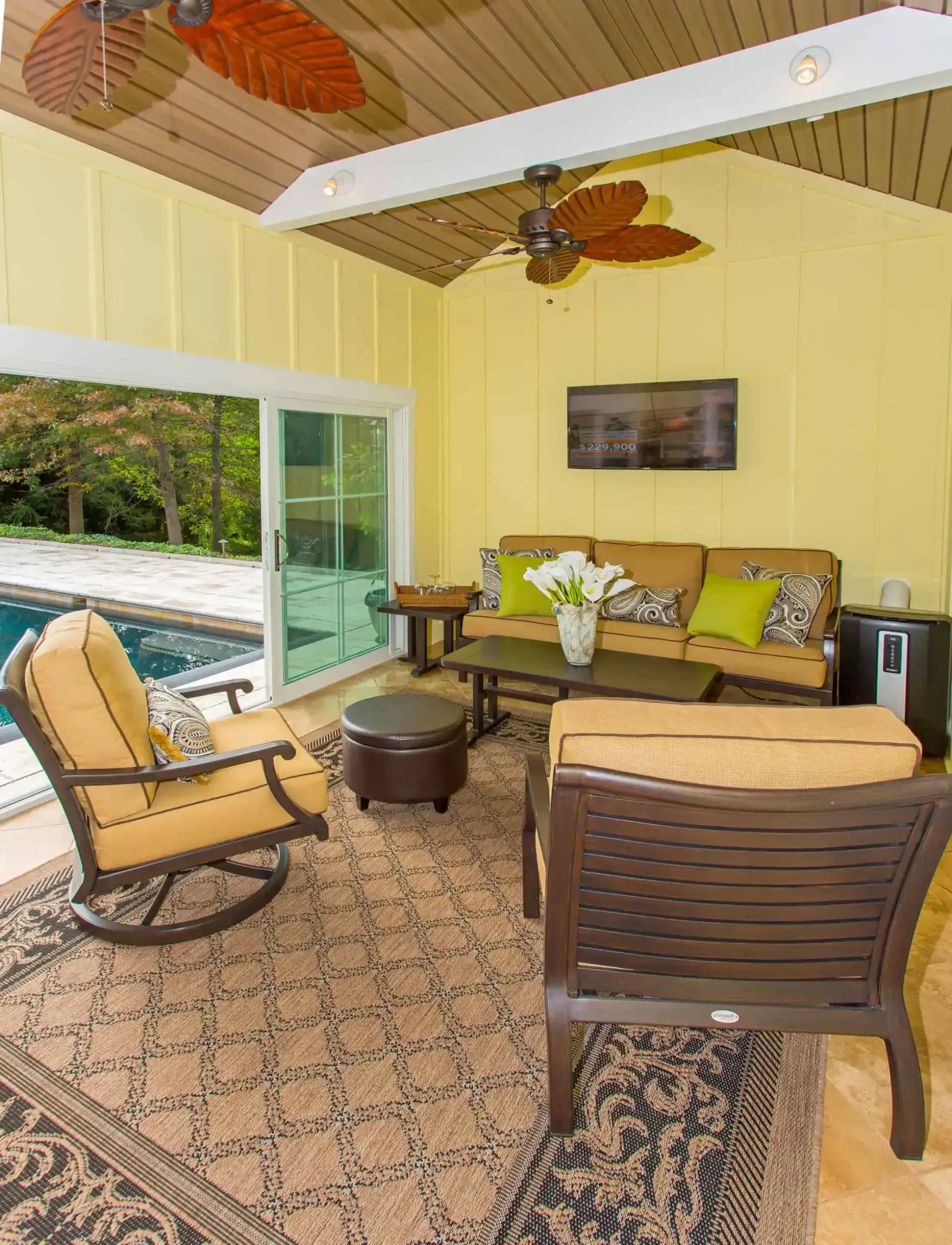 Covered patio with wicker seating, patterned rug, ceiling fan, and sliding door view of a pool.
