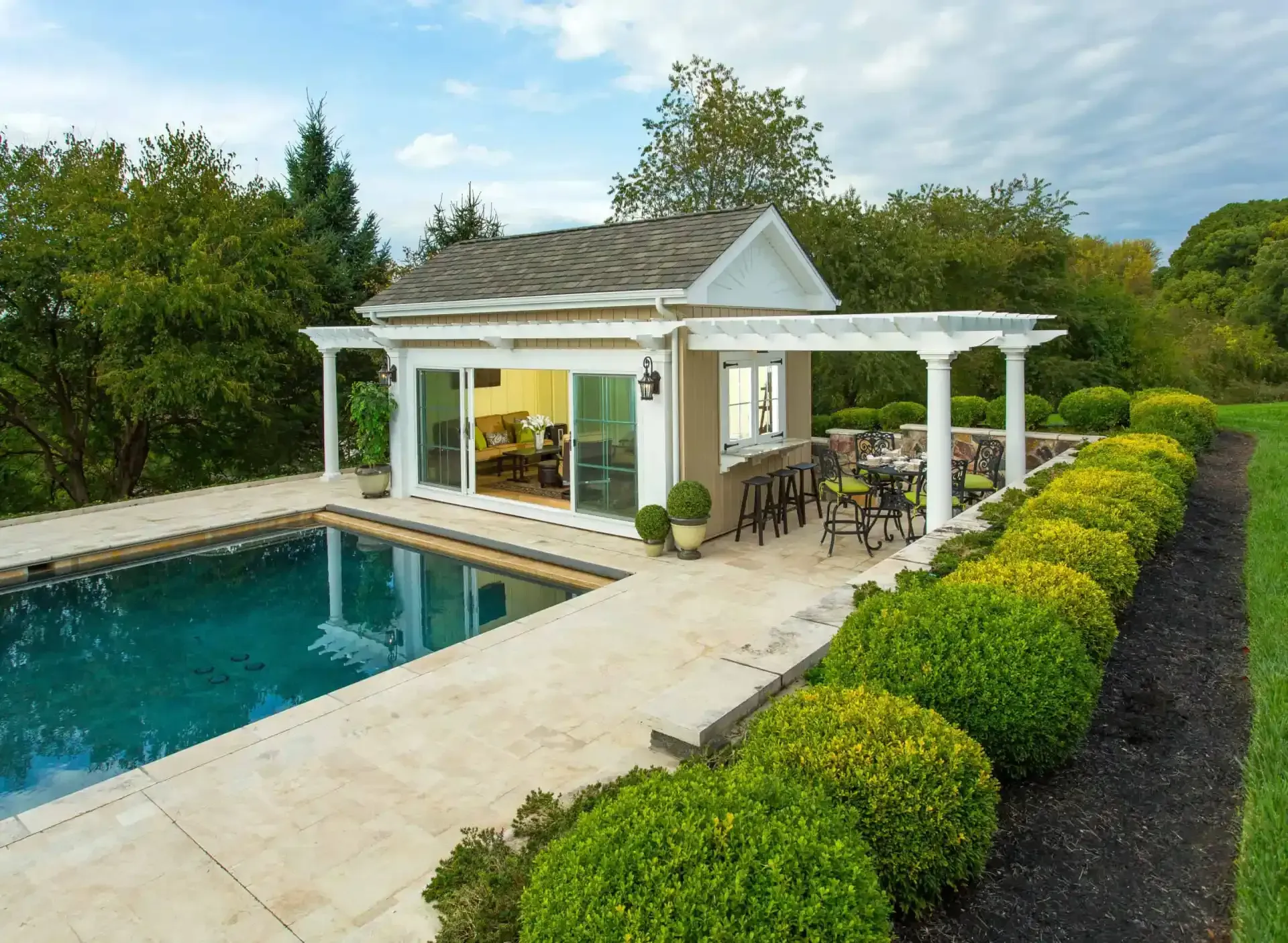 Poolside gazebo with white columns beside a turquoise pool and neatly trimmed hedges