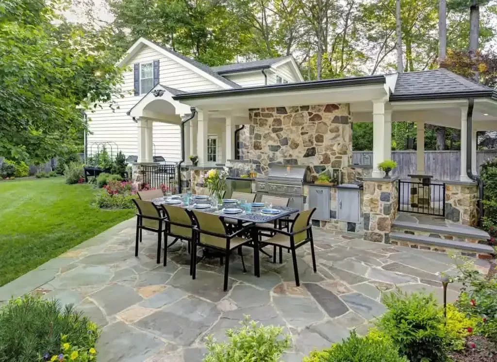 Stone patio with black dining table and chairs beside a white house and garden greenery