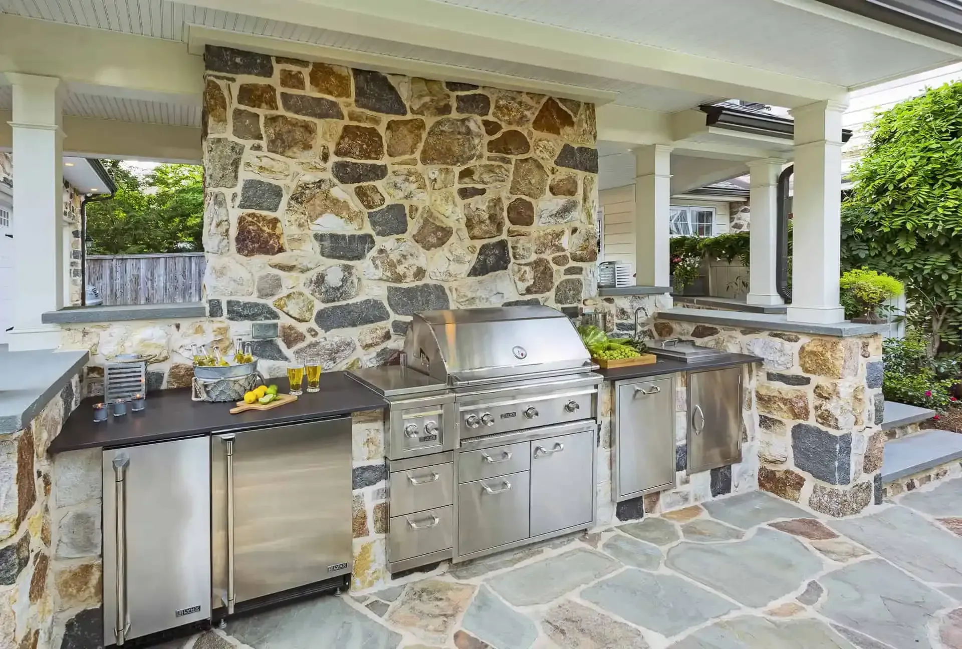 Outdoor stone patio kitchen with built-in grill, sink, and counter space under a covered porch