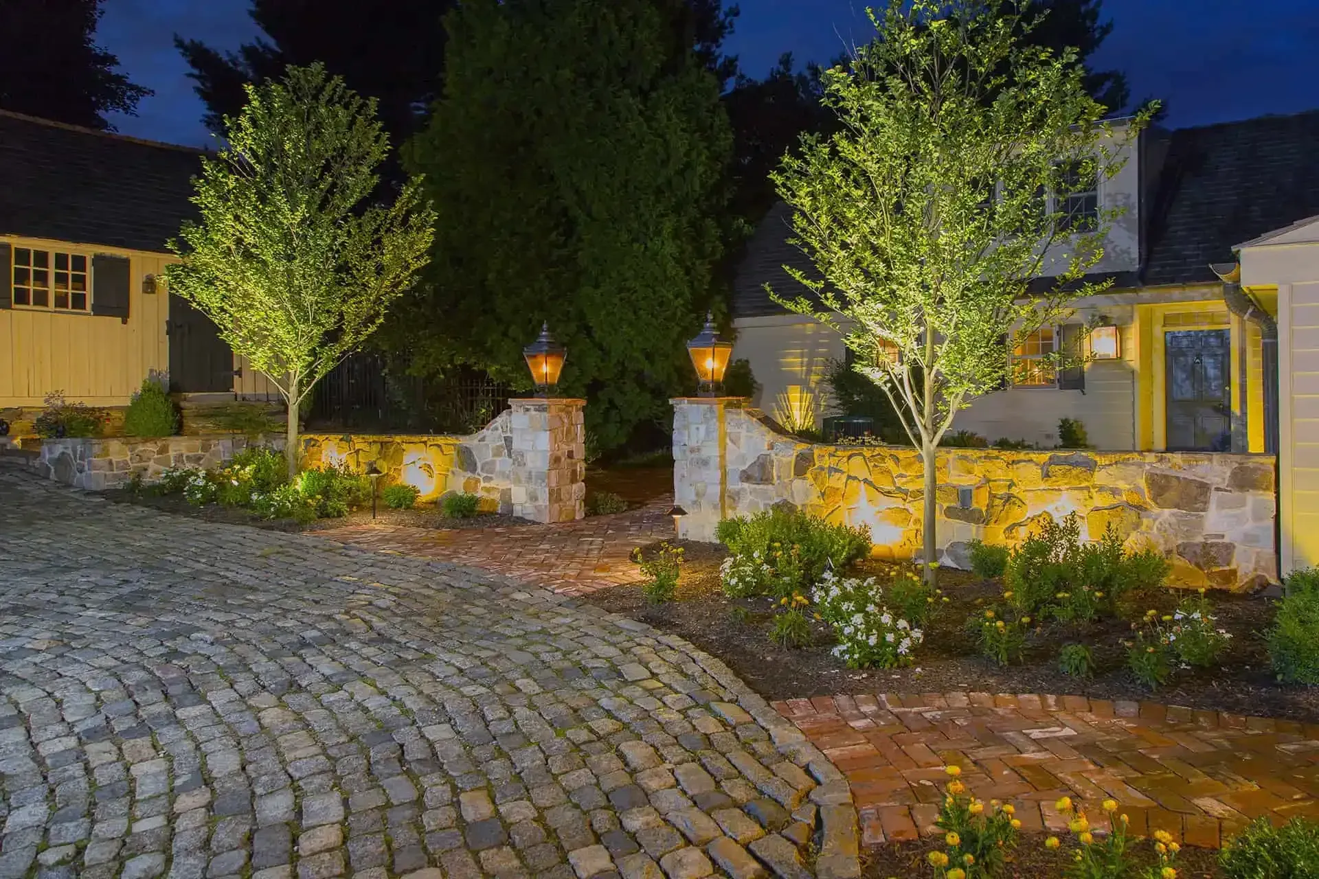Illuminated cobblestone driveway leading to a stone-walled house entrance at night
