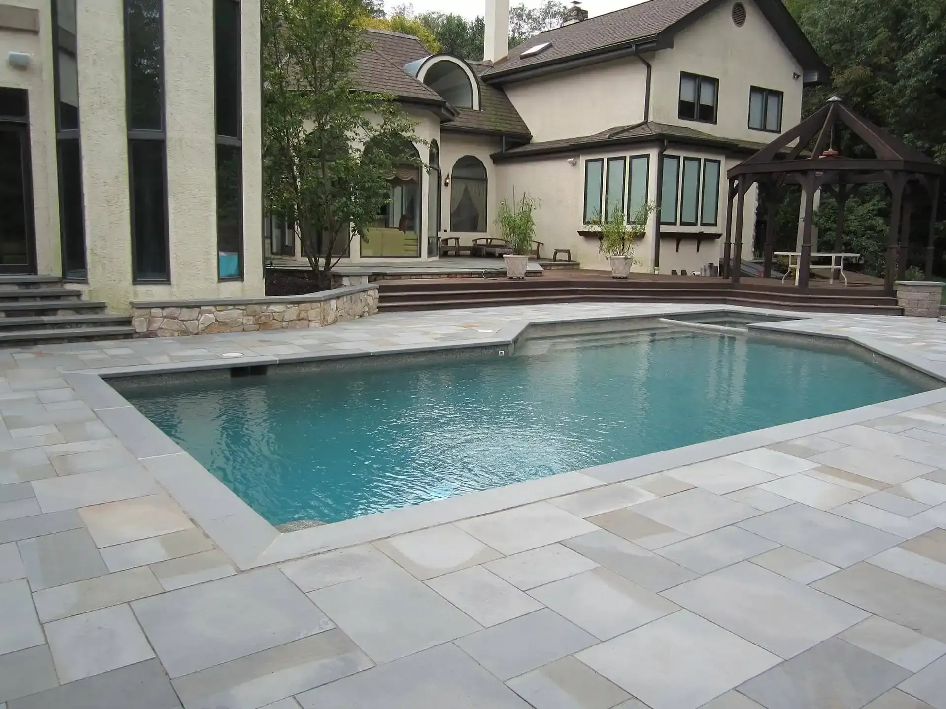 Backyard patio with a turquoise swimming pool beside a modern house and stone deck