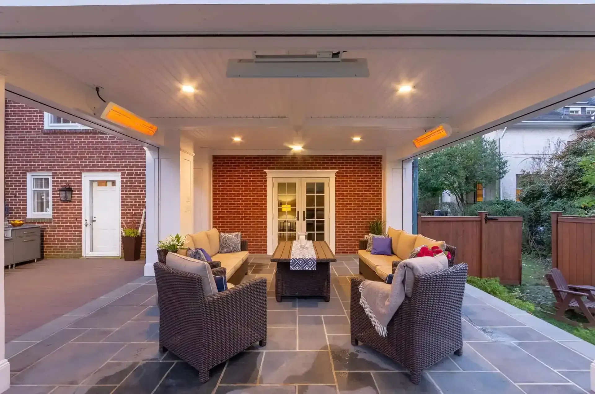 Covered patio with wicker seating, outdoor heater, and French doors opening to a brick house