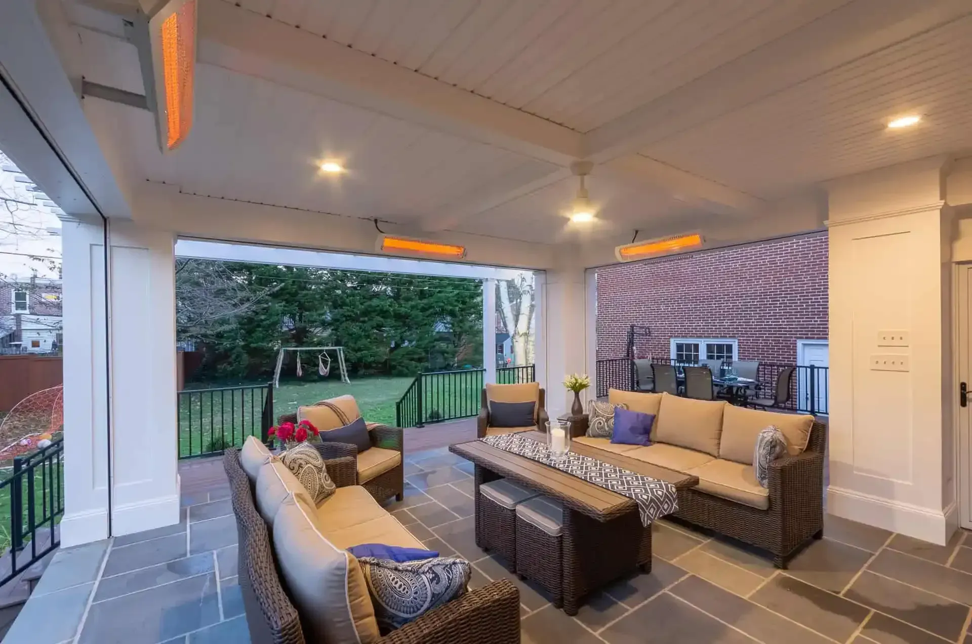Covered patio with cushioned seating, dining table, and backyard view at dusk