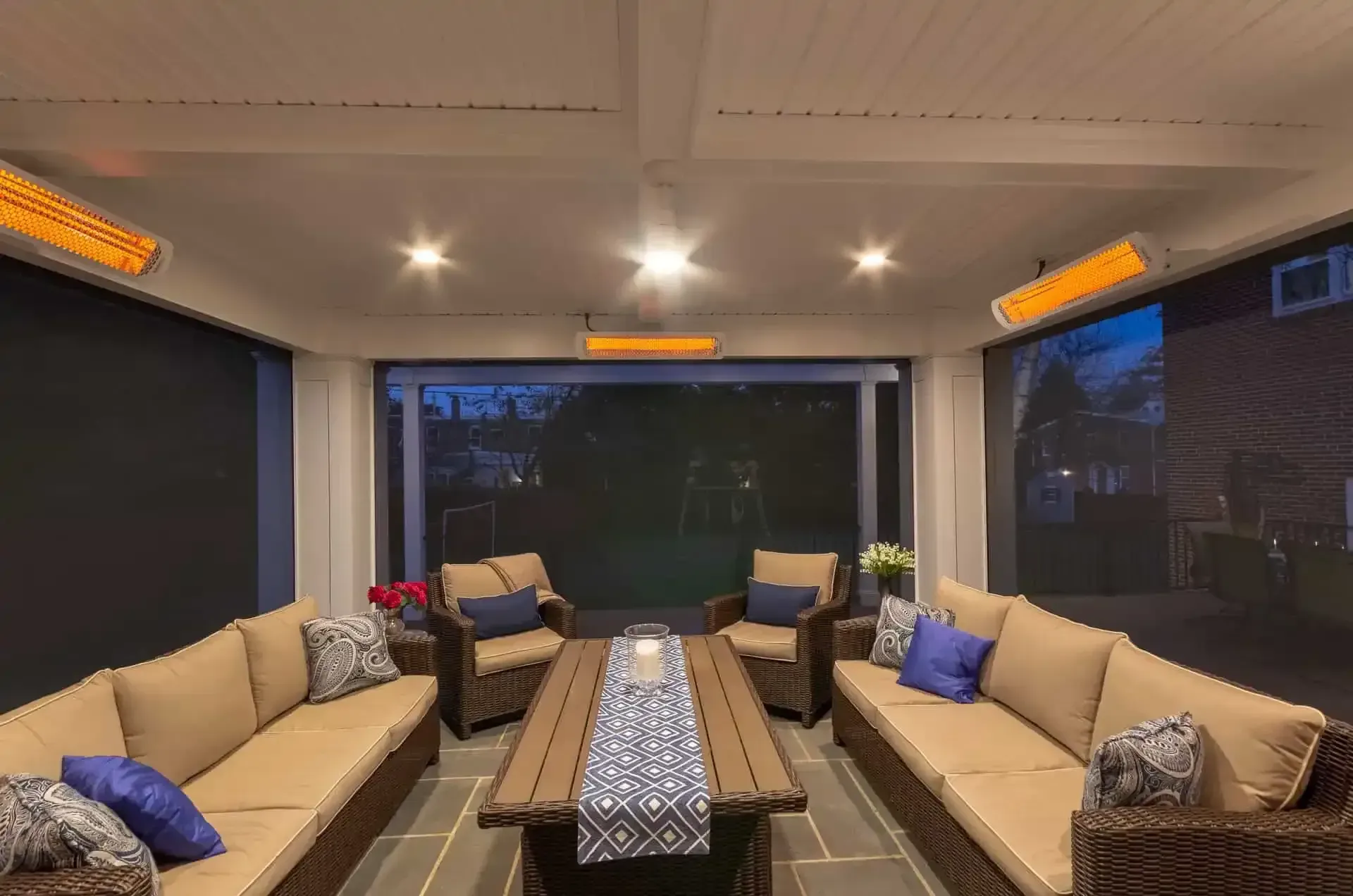 Cozy enclosed patio lounge with beige sofas, a central table, and warm ceiling lights at dusk