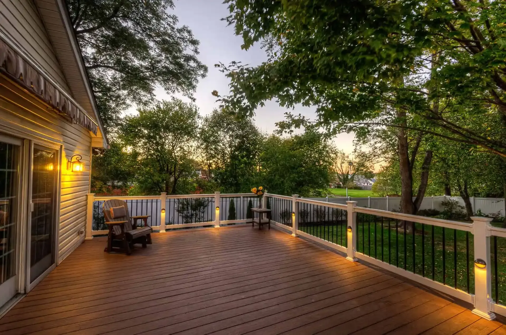 Wooden deck at dusk with warm string lights, railing, and trees overlooking a yard