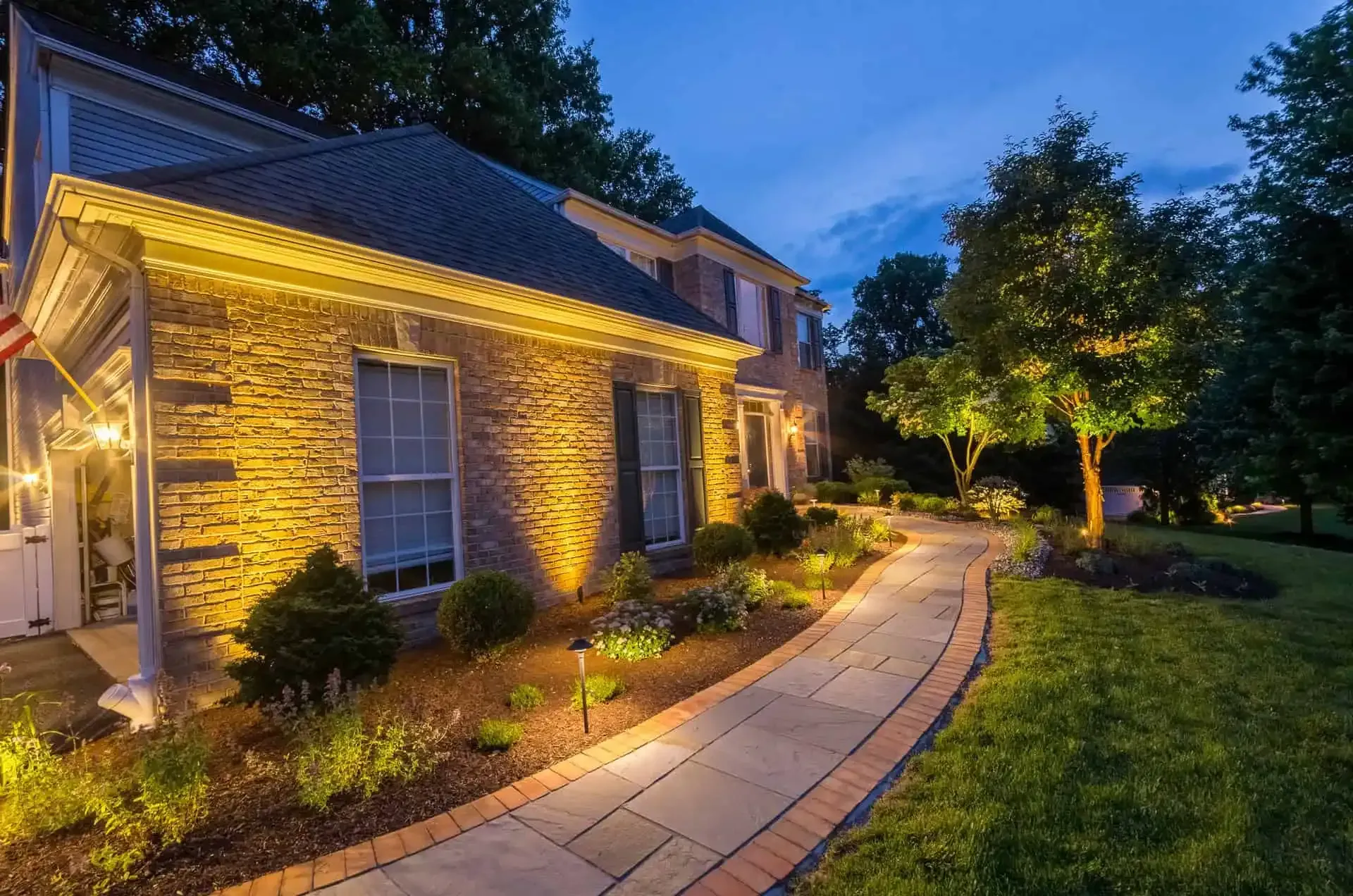 Stone house with warm exterior lights and a curving walkway at dusk