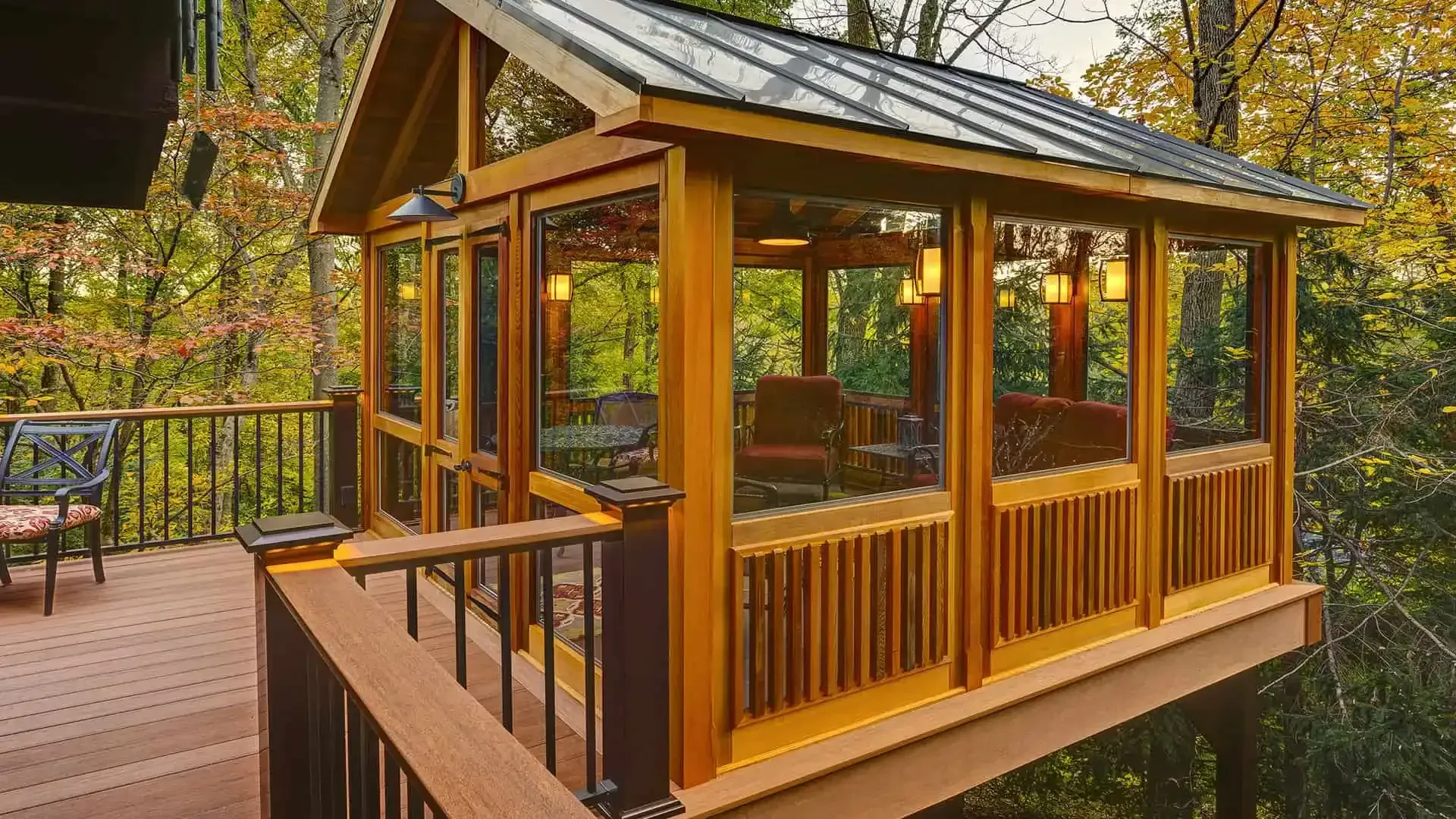 Wooden cabin deck with large windows, surrounded by autumn forest foliage