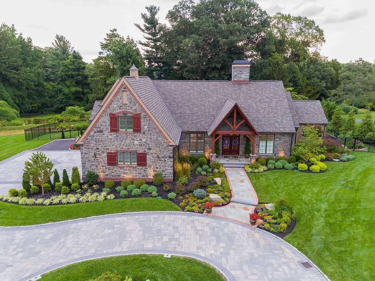 Stone house with a curved driveway, landscaped garden, and trees around it