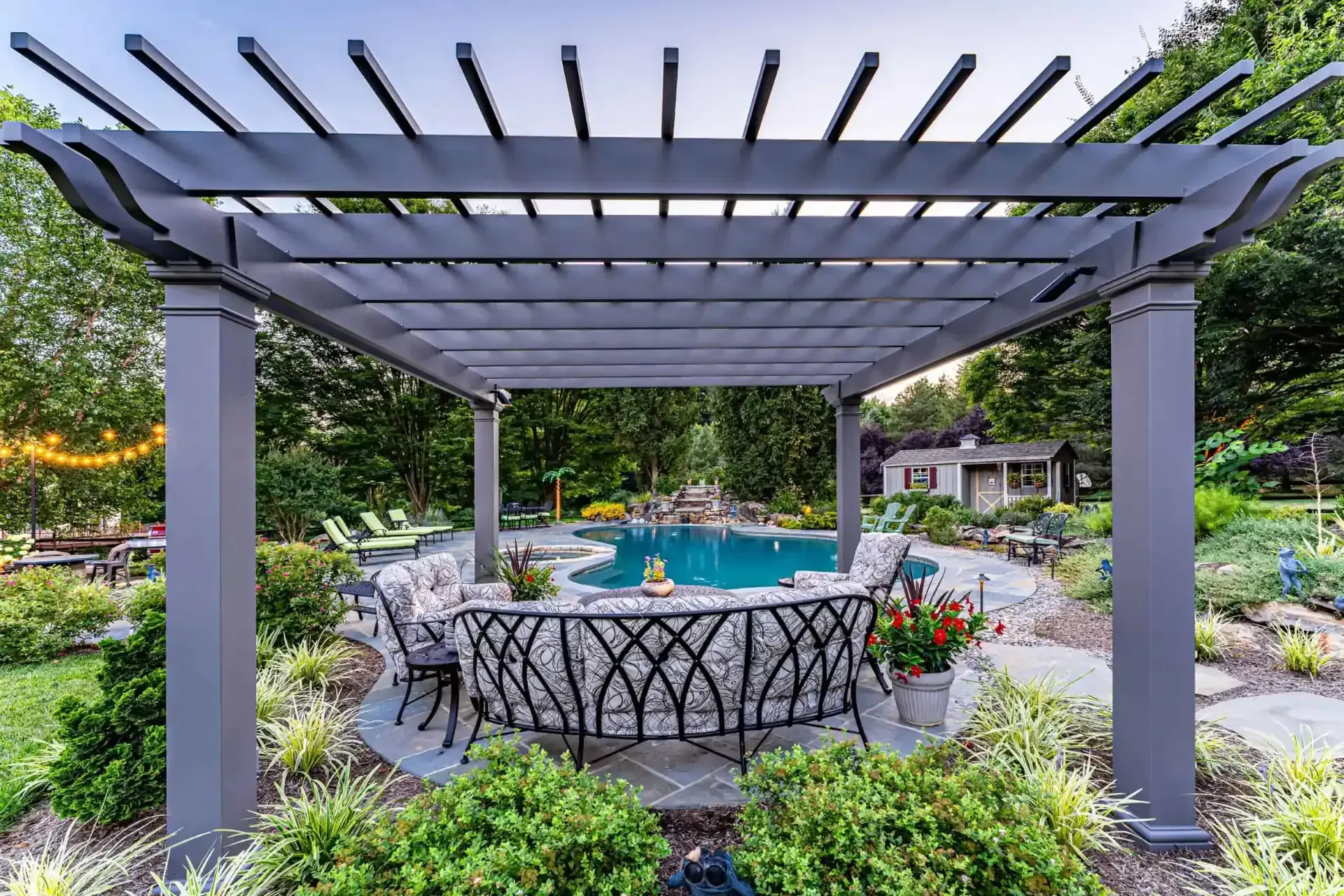 Pergola over a landscaped poolside patio with wicker seating and flowers
