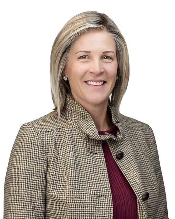 Smiling professional in a beige blazer over a burgundy top against a white background