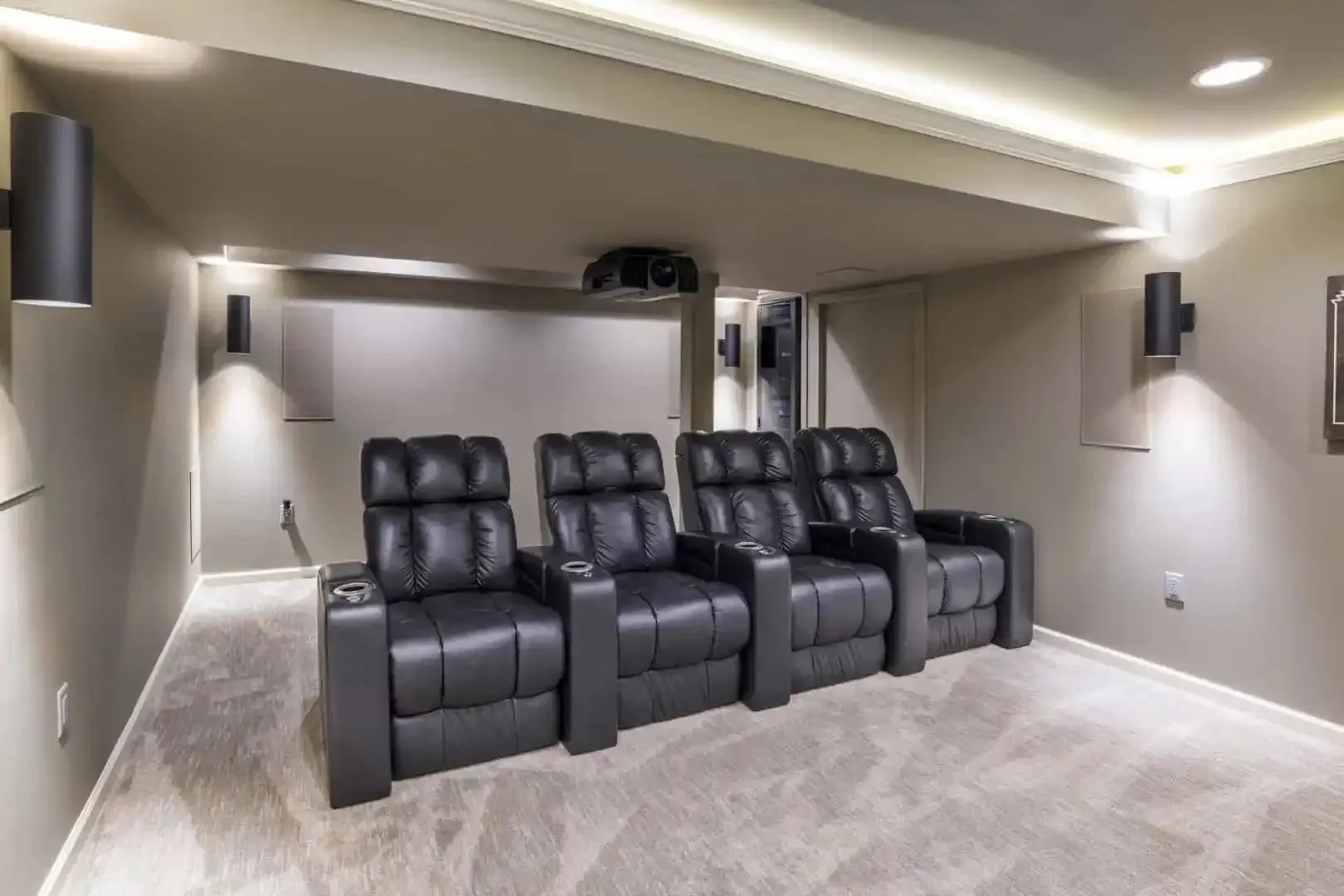 Home theater room with four black recliner seats, wall sconces, and beige carpet