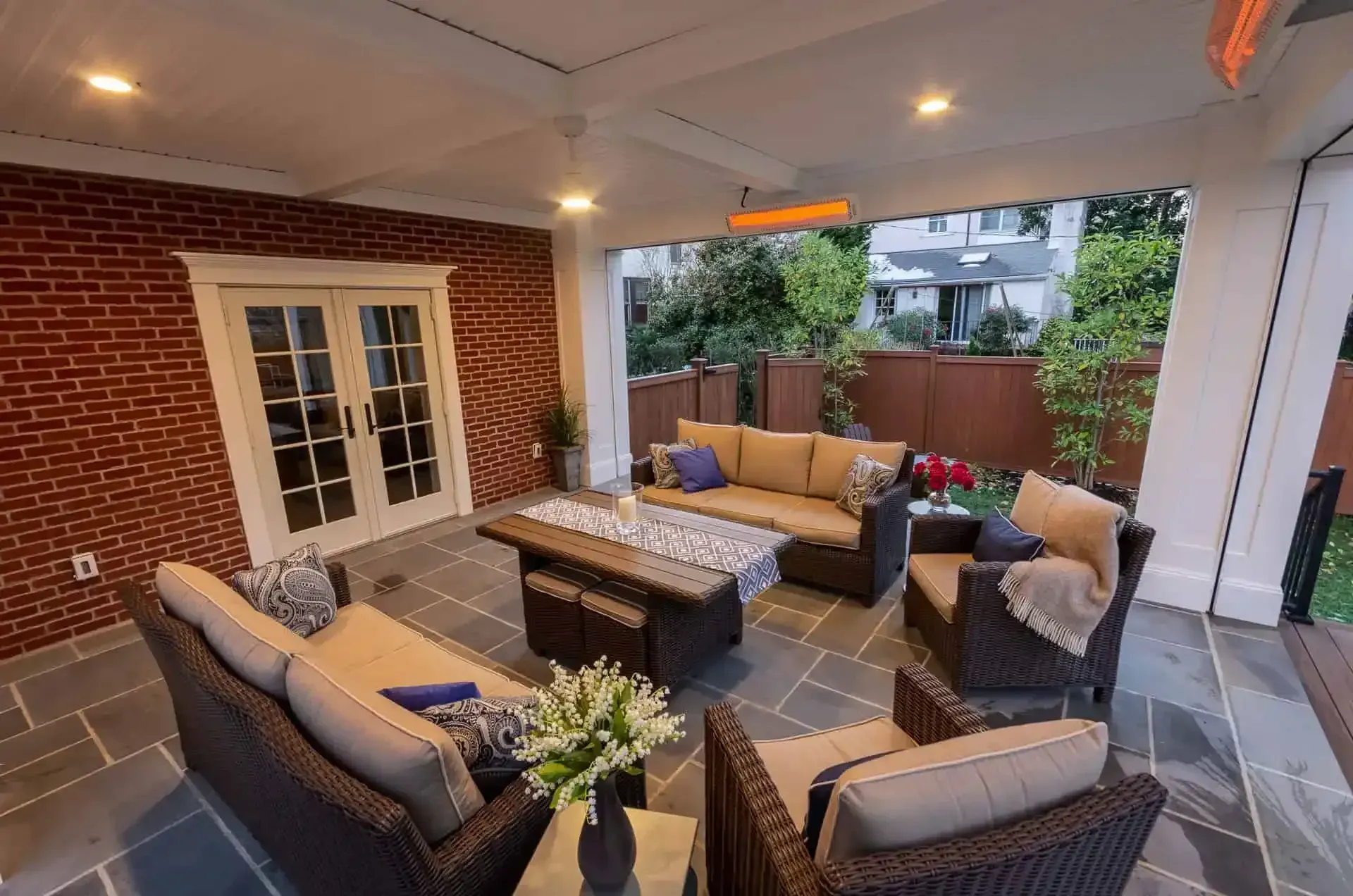 Covered patio with wicker seating, coffee table, and string lights beside a brick house