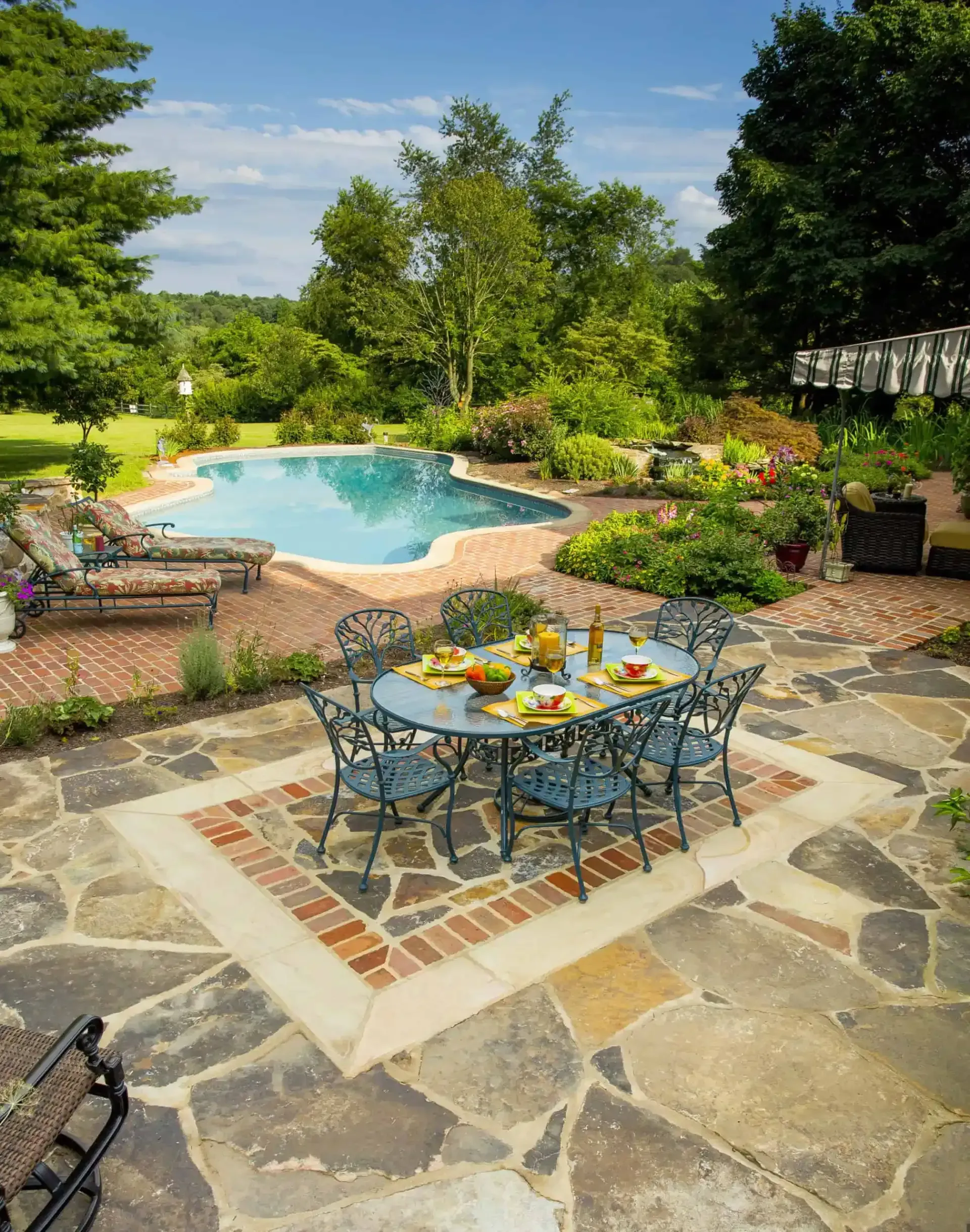 Patio dining set beside a turquoise backyard pool, surrounded by lush garden greenery