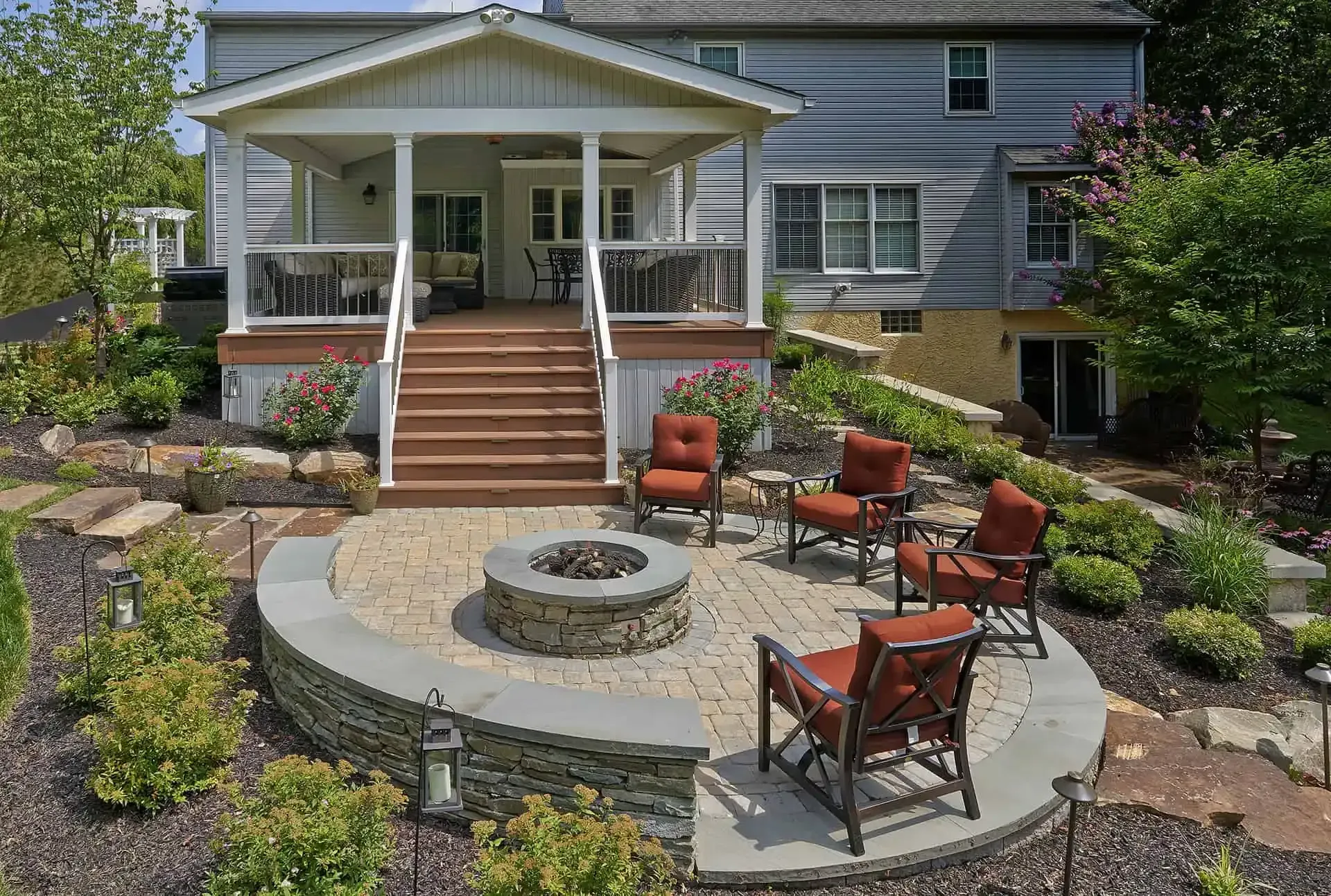 Patio with fire pit, red chairs, and stone landscaping in front of a white porch on a gray house