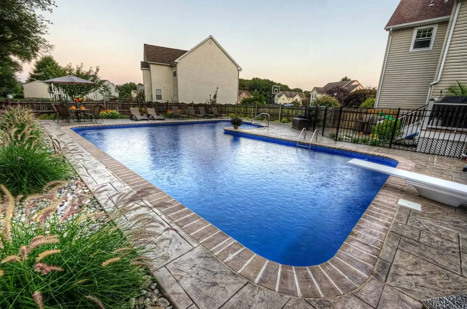 Backyard swimming pool with blue water, stone deck, and surrounding houses at sunset