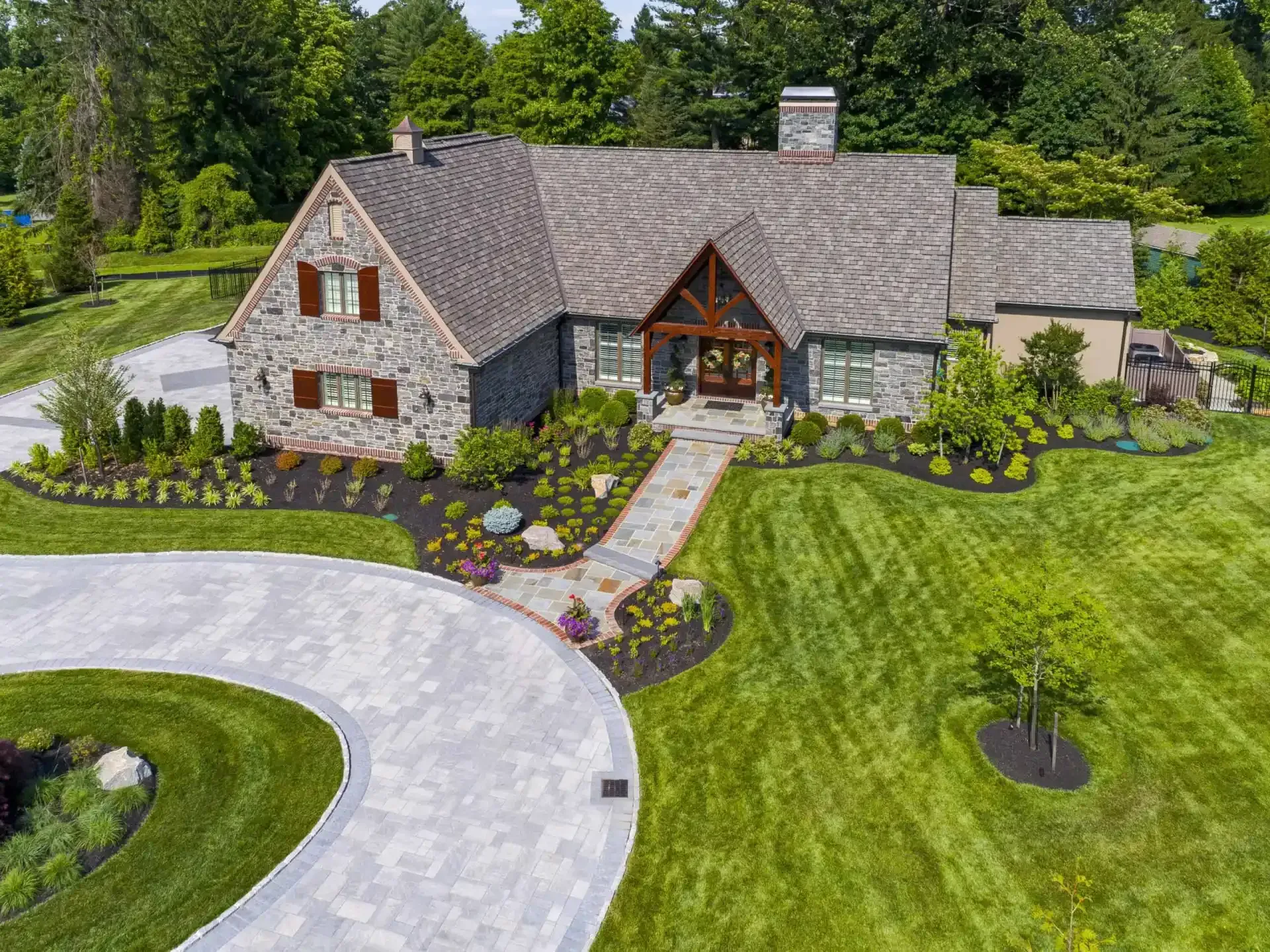 Aerial view of a stone house with a manicured lawn, curved driveway, and landscaped garden.
