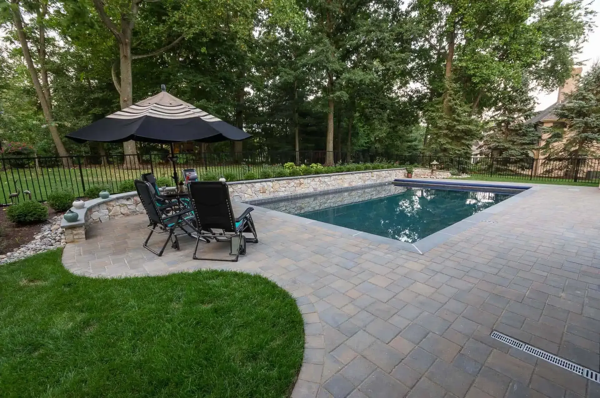 Backyard patio with a rectangular in-ground pool, lounge chairs, umbrella, and surrounding trees