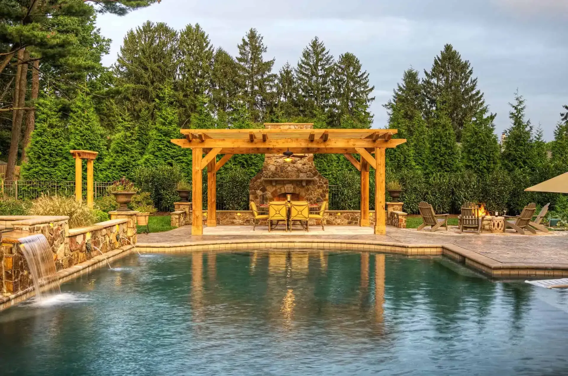 Resort pool with a wooden pergola, stone waterfalls, and trees in the background