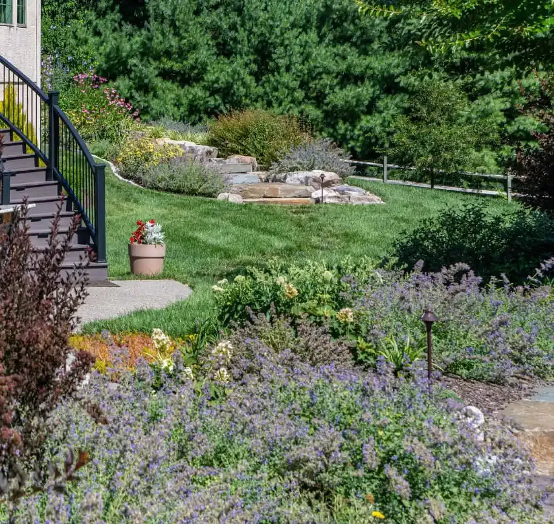 Backyard garden with stone steps, flowering shrubs, lawn, and a landscaped rock area