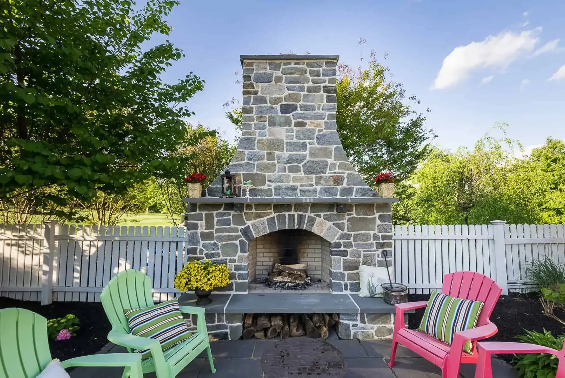 Stone outdoor fireplace with pink and green chairs in a backyard patio