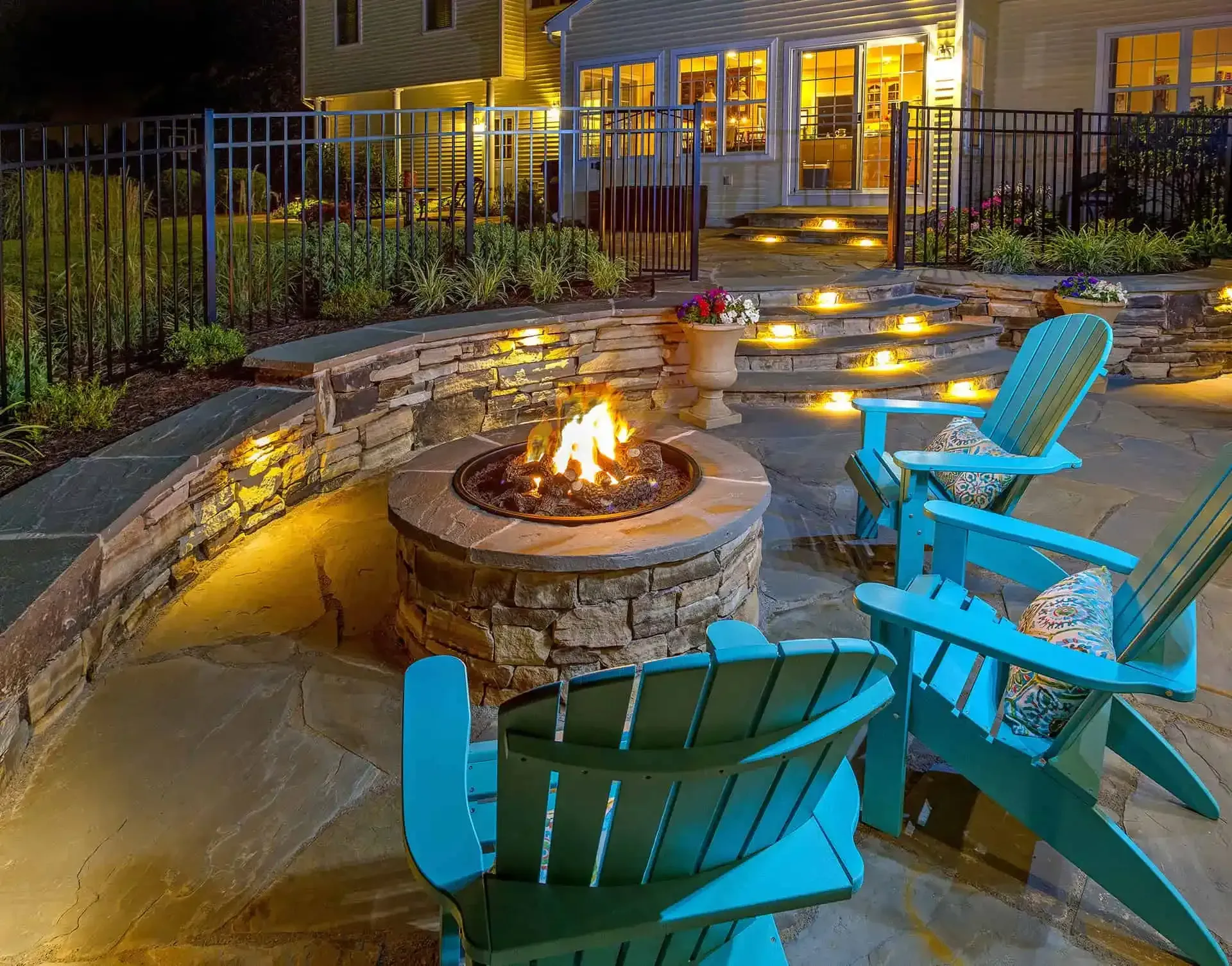 Backyard fire pit at night with blue chairs and warm patio lights