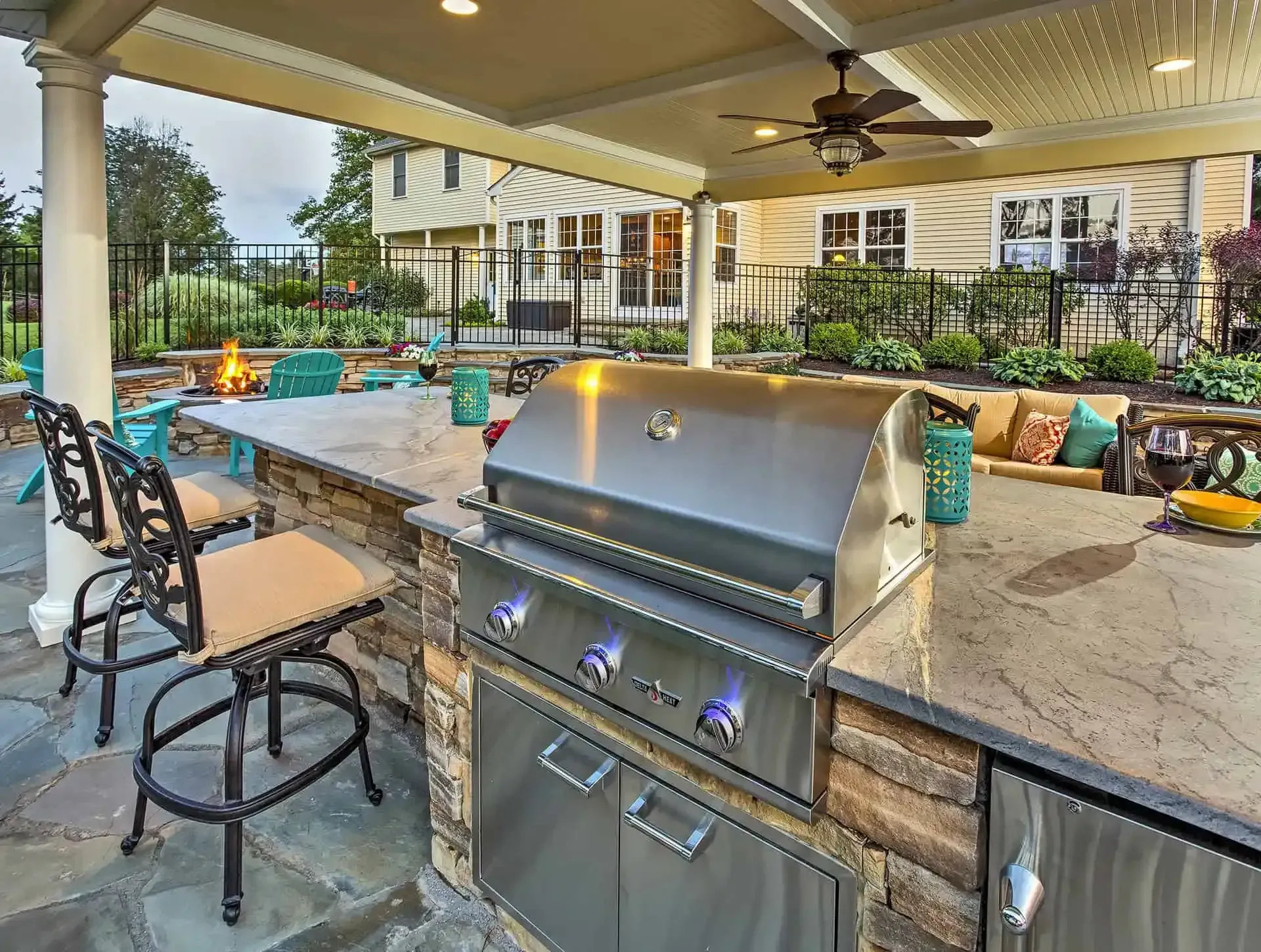 Covered outdoor patio with a built-in grill, stone bar seating, and a fire pit by a pool area