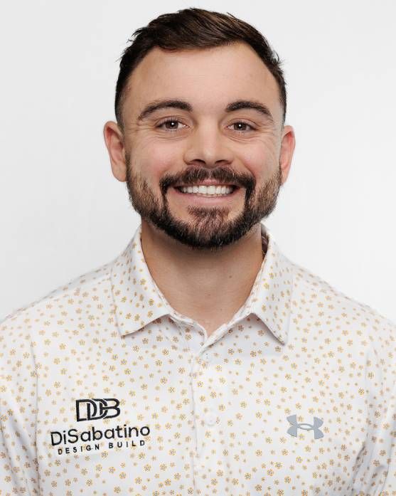 A smiling man in a white patterned shirt against a light background, wearing a Disbatto logo.