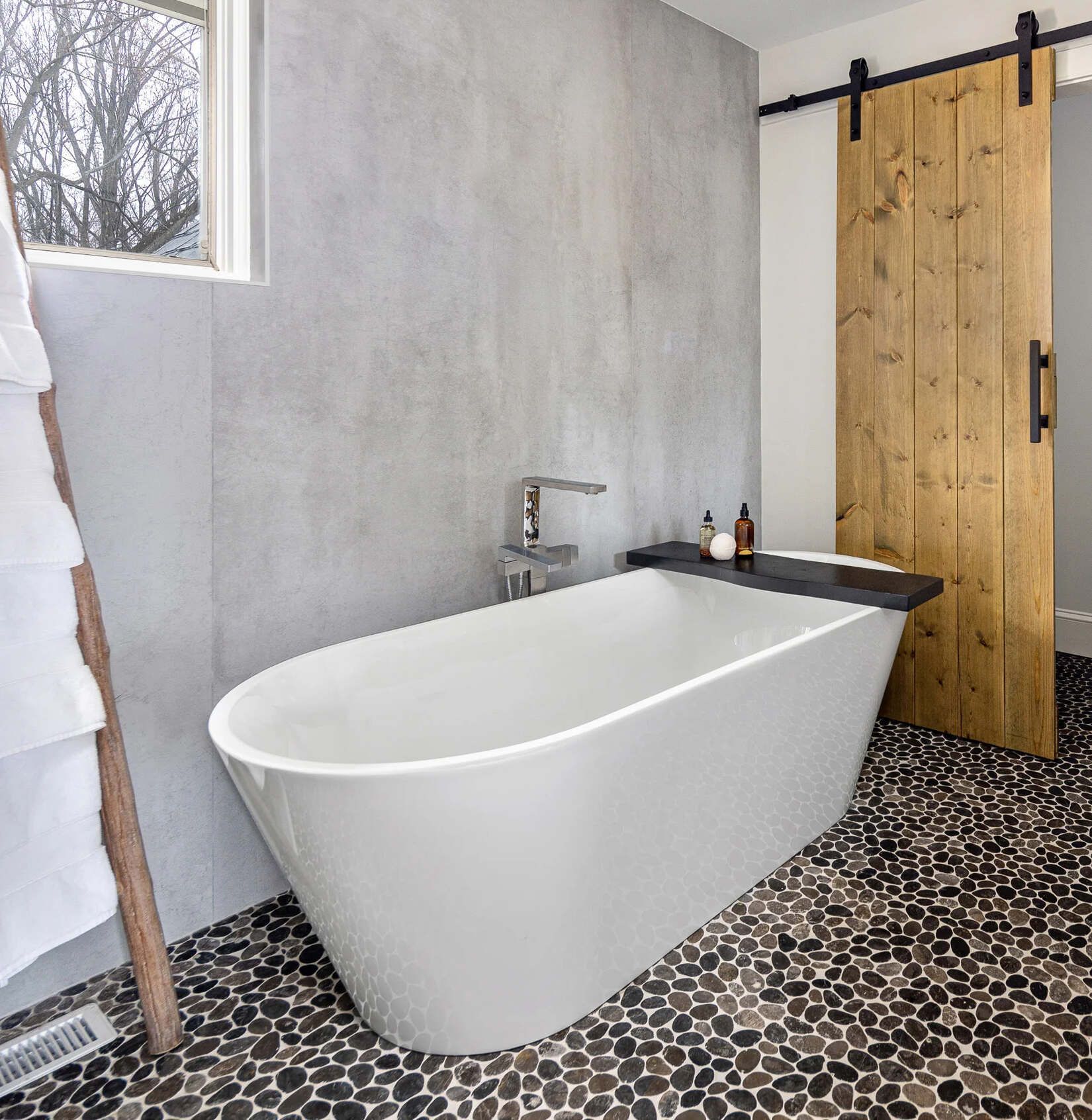 Modern bathroom with freestanding white tub, black-and-white tile floor, and wooden sliding door