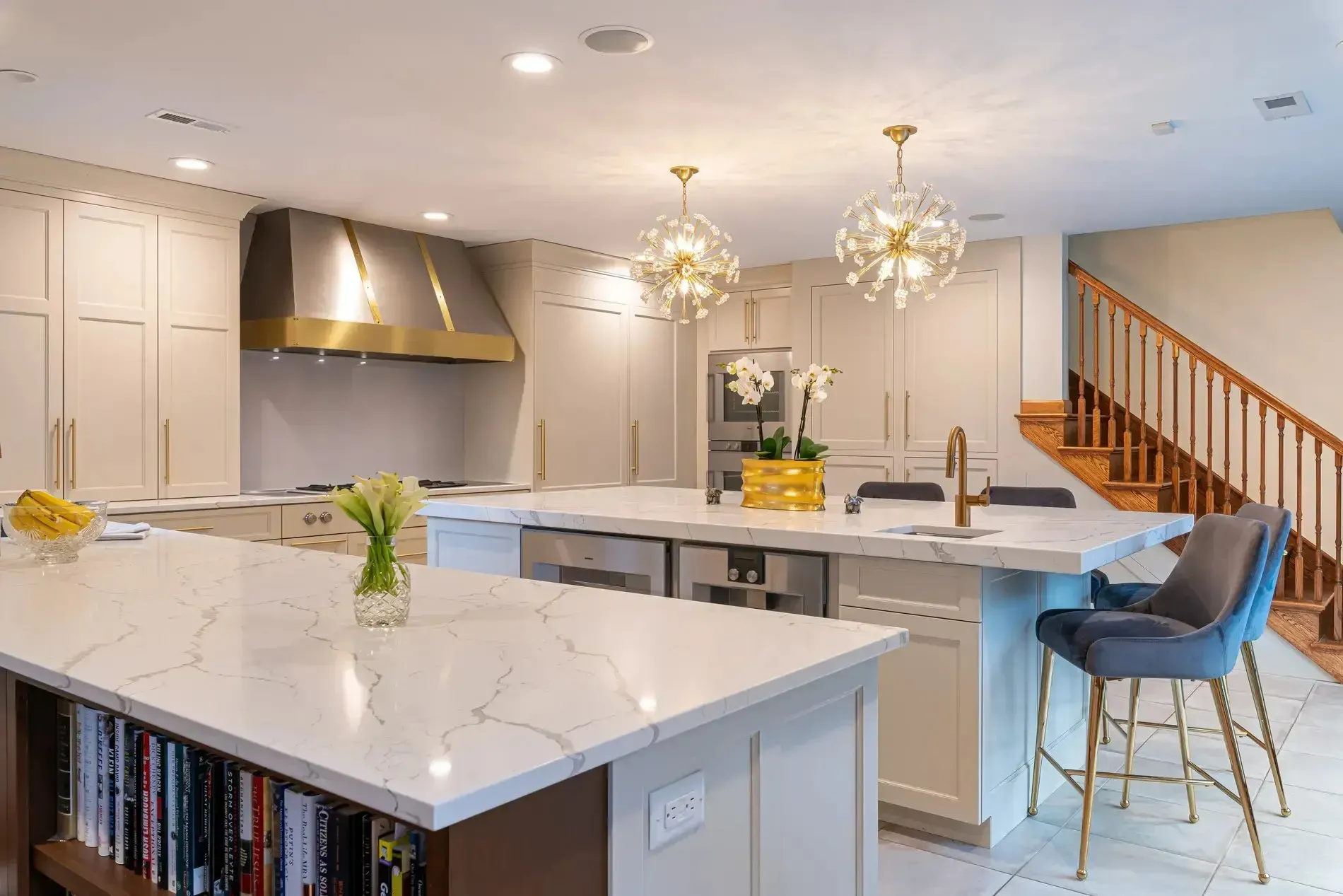 Bright modern kitchen with marble island, stainless range hood, pendant lights, and blue bar stool near stairs
