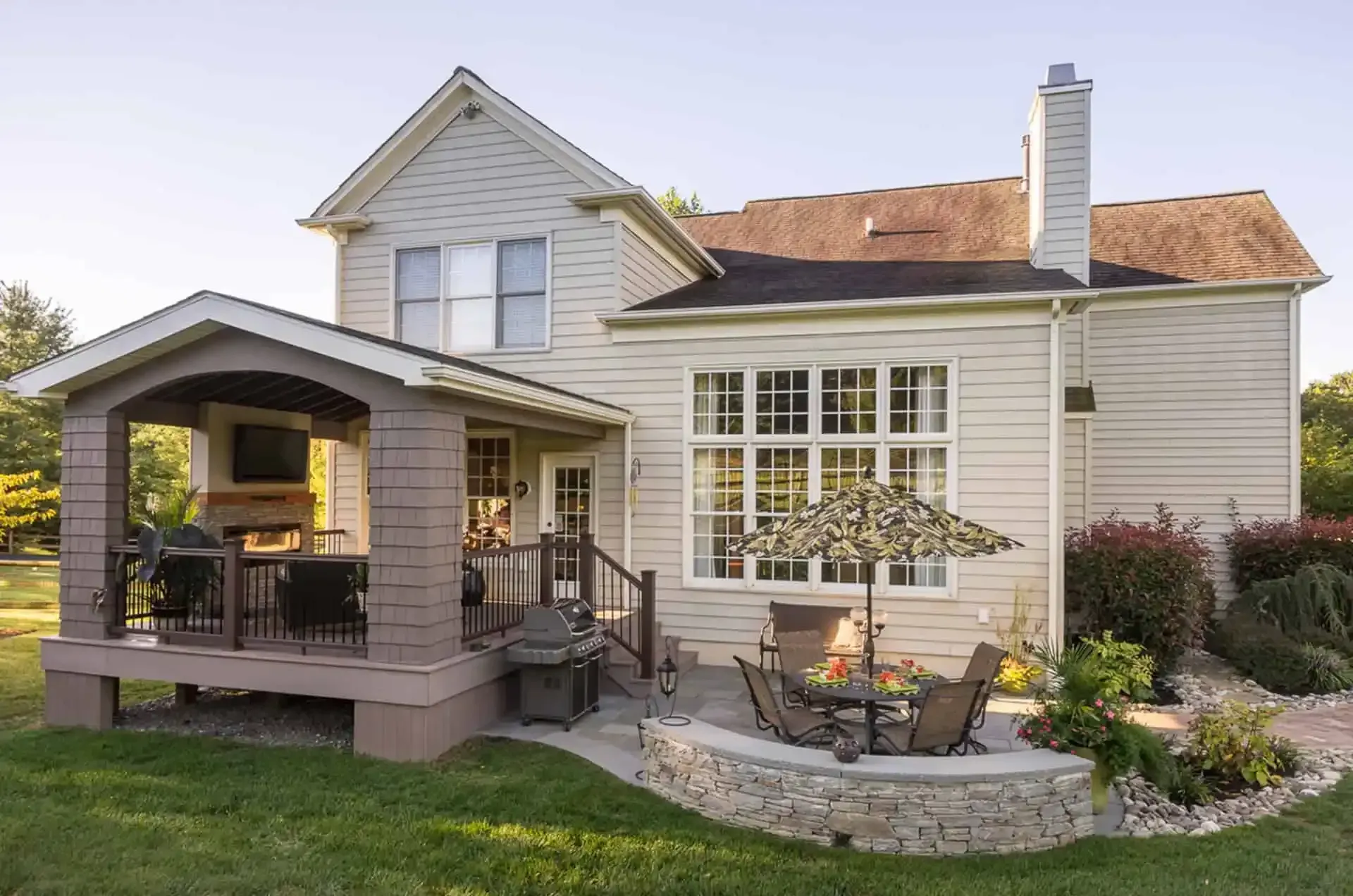 Rear view of a white house with a covered patio, deck, and landscaped backyard seating area