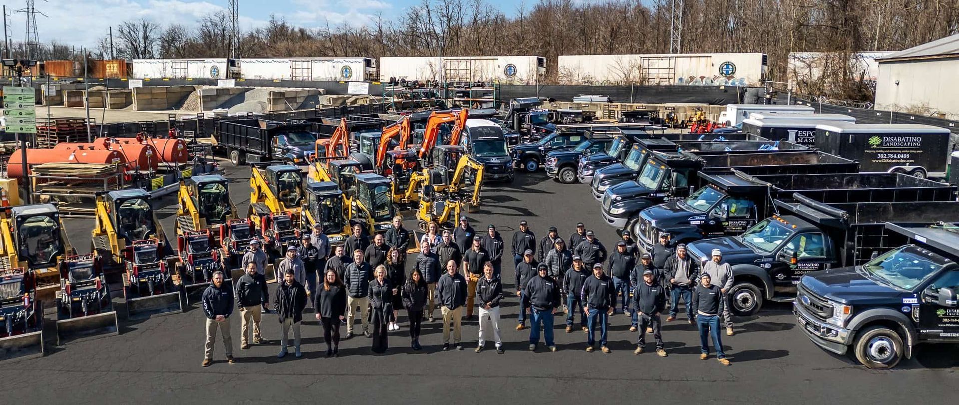 People gathered among rows of blue and orange utility trucks in a large outdoor lot.