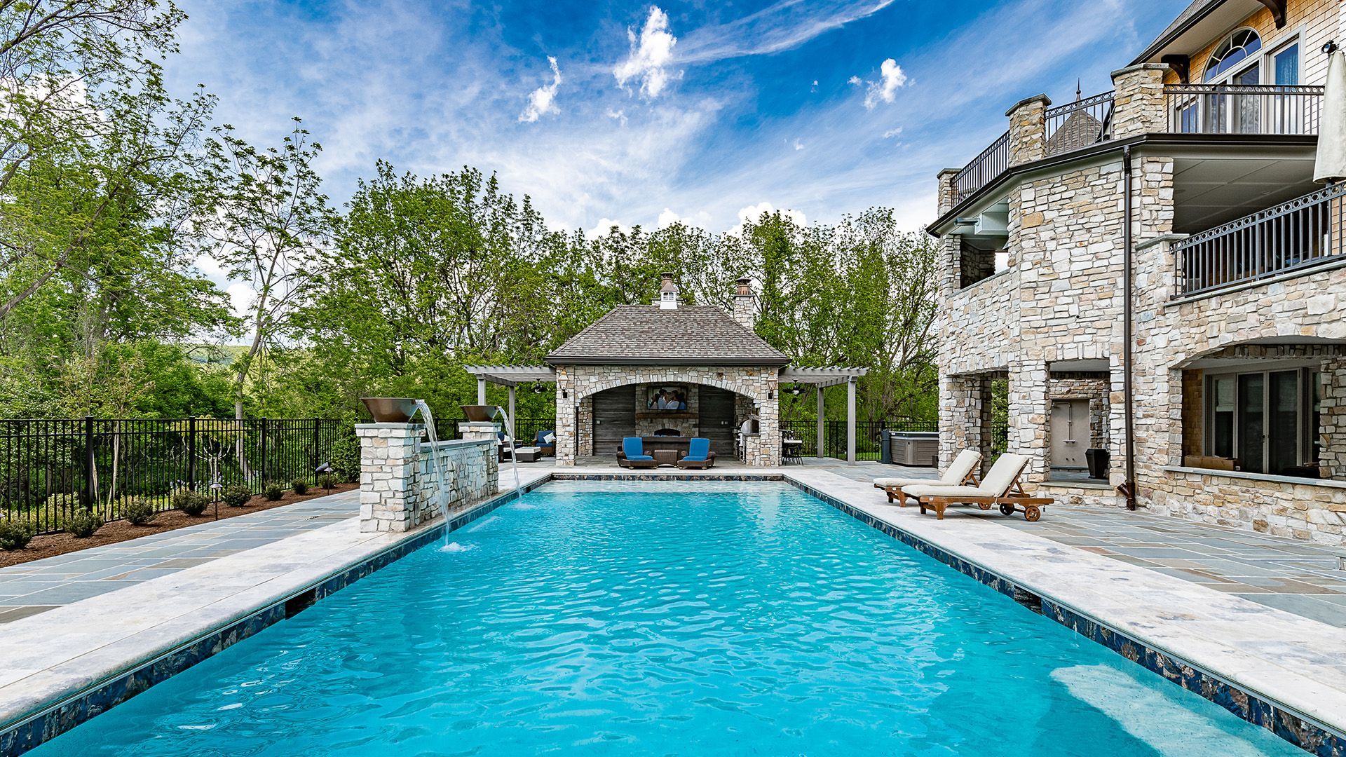 Luxury backyard with blue swimming pool, stone patio, and a house with an outdoor lounge area