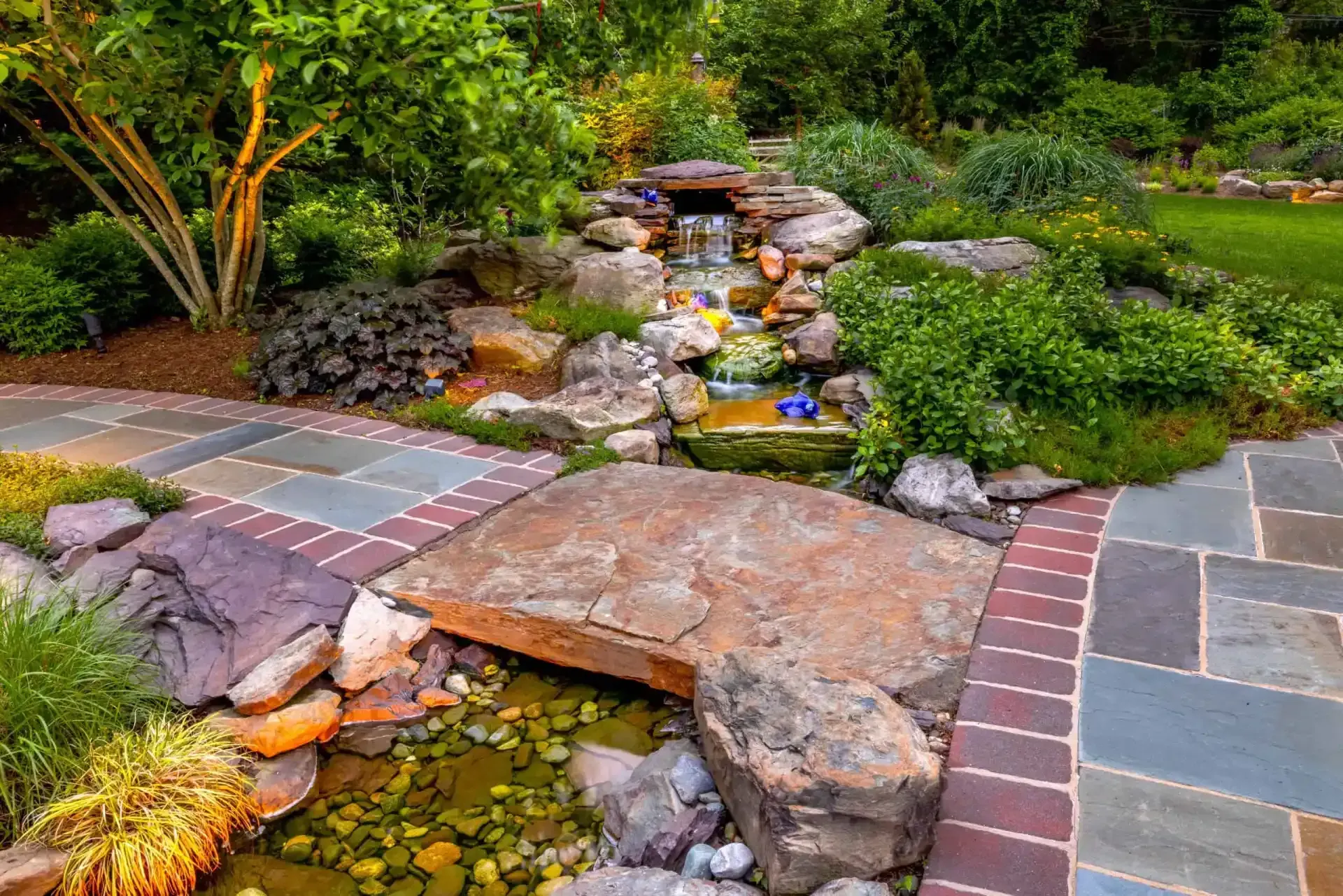 Garden path with a small stone stream, lush greenery, and brick and slate paving