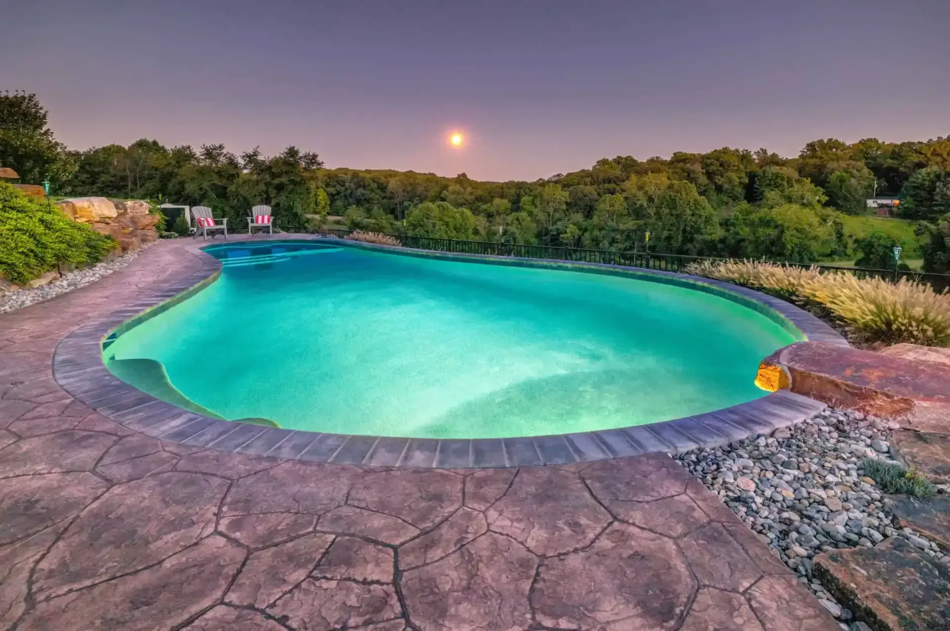 Turquoise infinity pool at sunset, surrounded by stone decking and lush greenery.