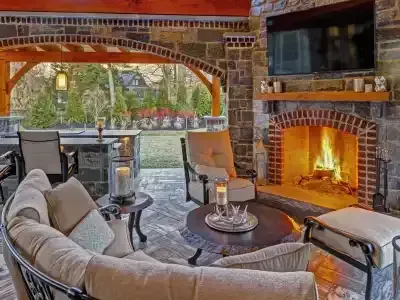 Cozy patio with cushioned seating and a lit brick fireplace beside a covered outdoor dining area.