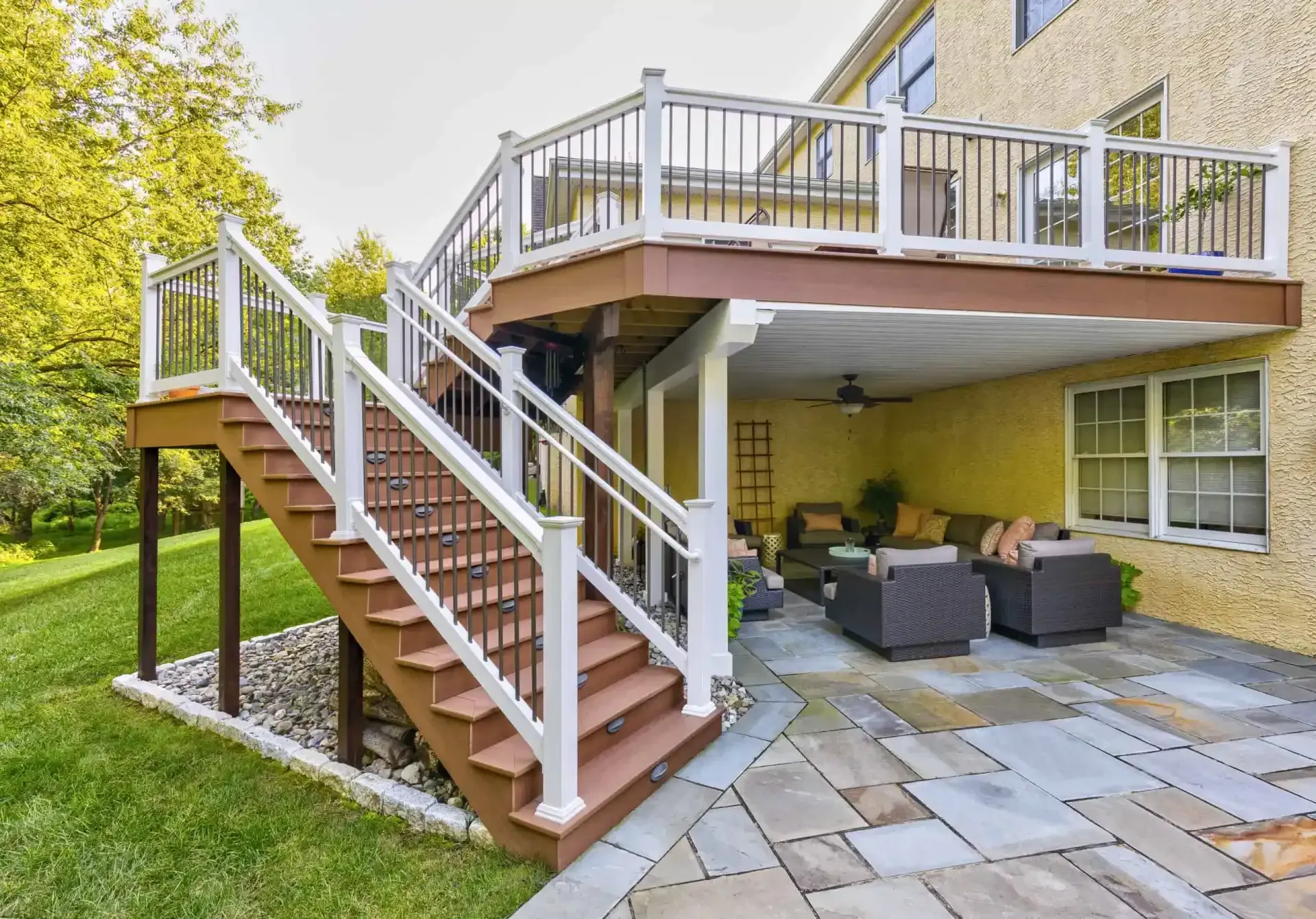 Backyard patio with wooden stairs leading to an elevated deck and outdoor seating on stone paving