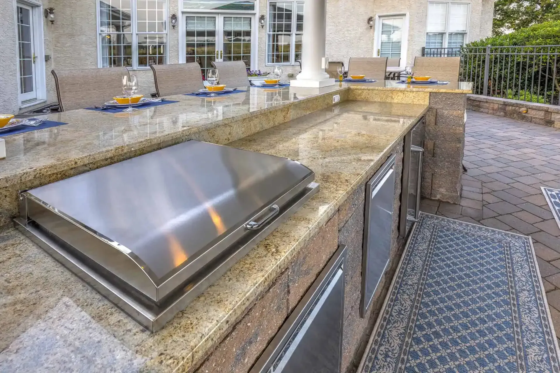 Outdoor stone patio kitchen with built-in grill and stainless steel countertop ליד seating area