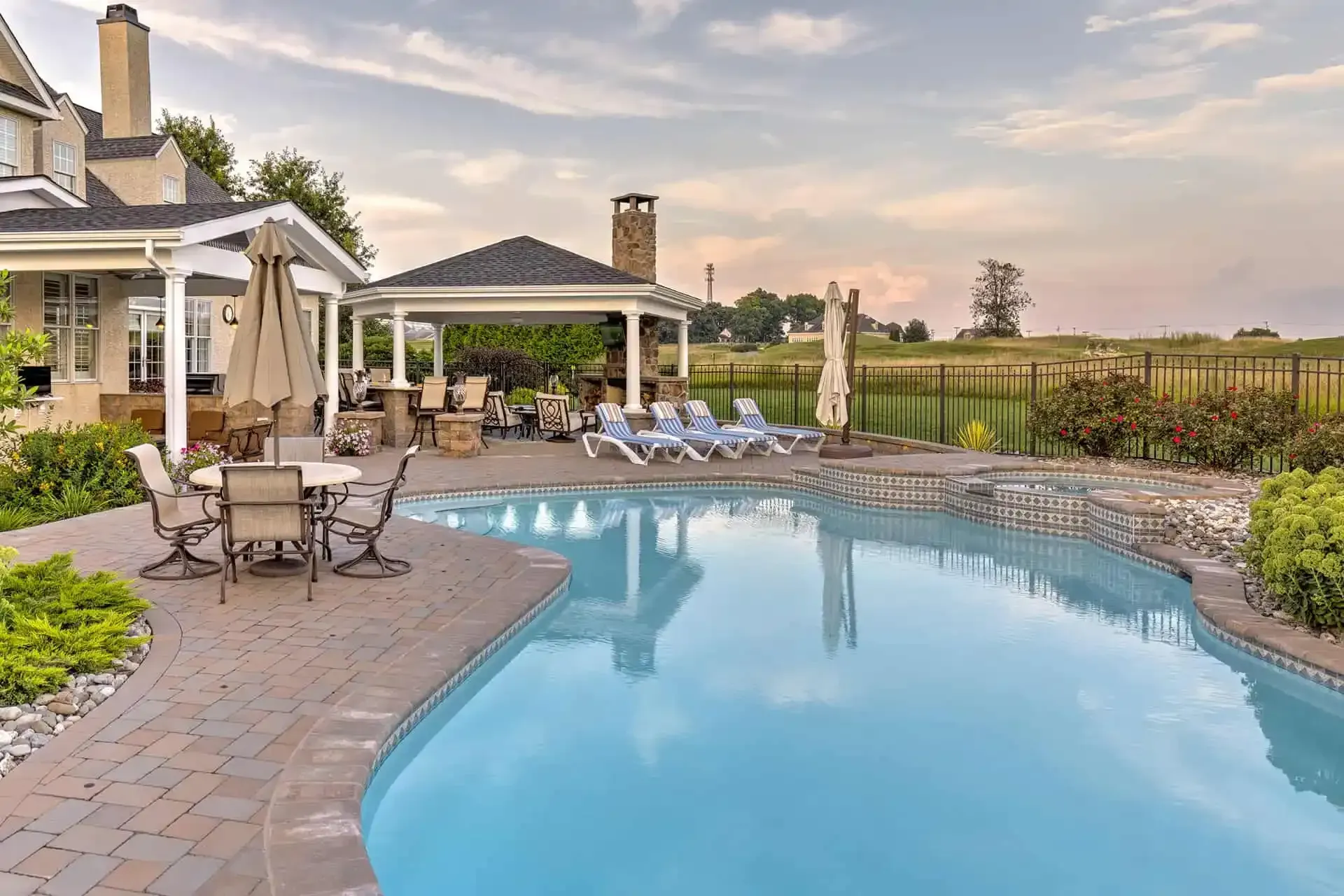 Backyard pool and patio with lounge chairs, stone deck, and sunset sky