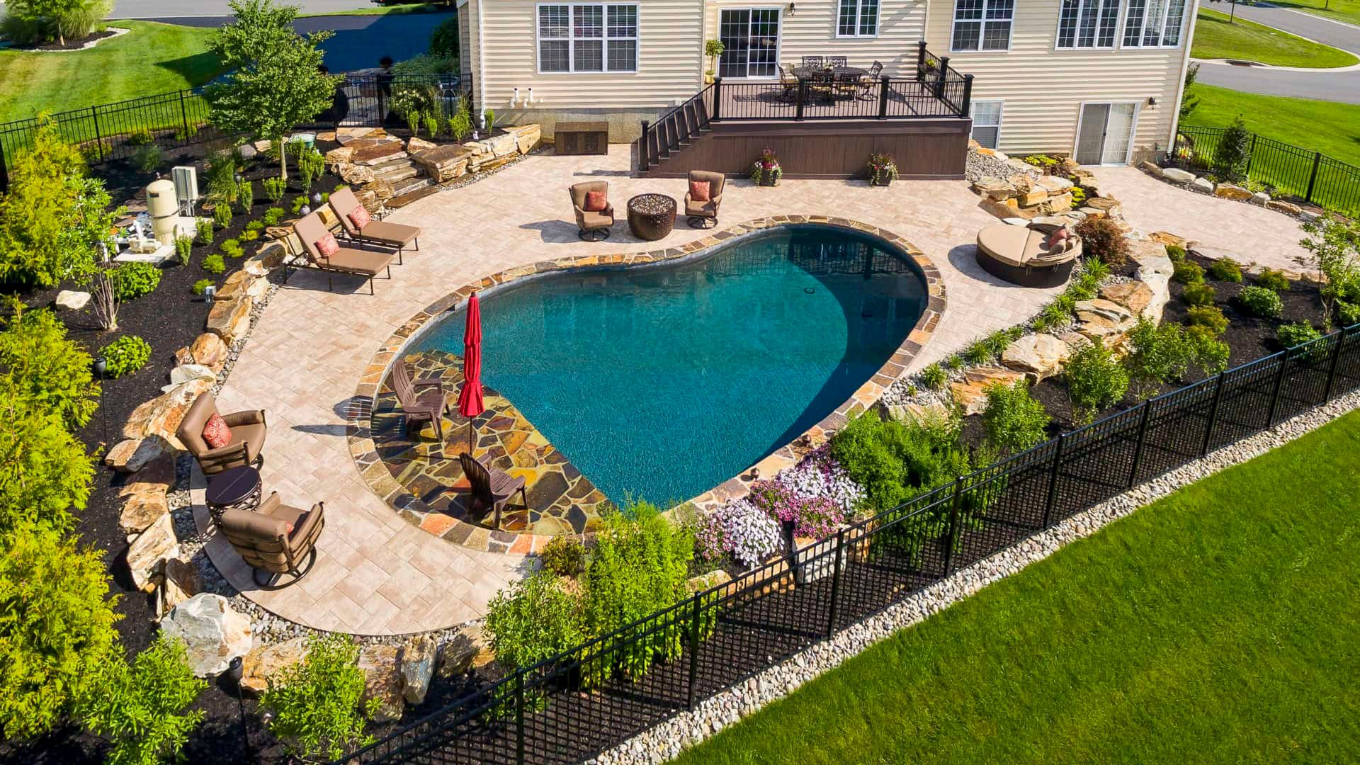 Backyard patio with a kidney-shaped swimming pool, lounge chairs, umbrellas, and a house in the background