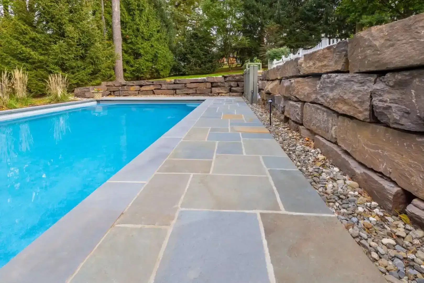 Poolside stone patio beside a bright blue swimming pool, with a stacked stone retaining wall.