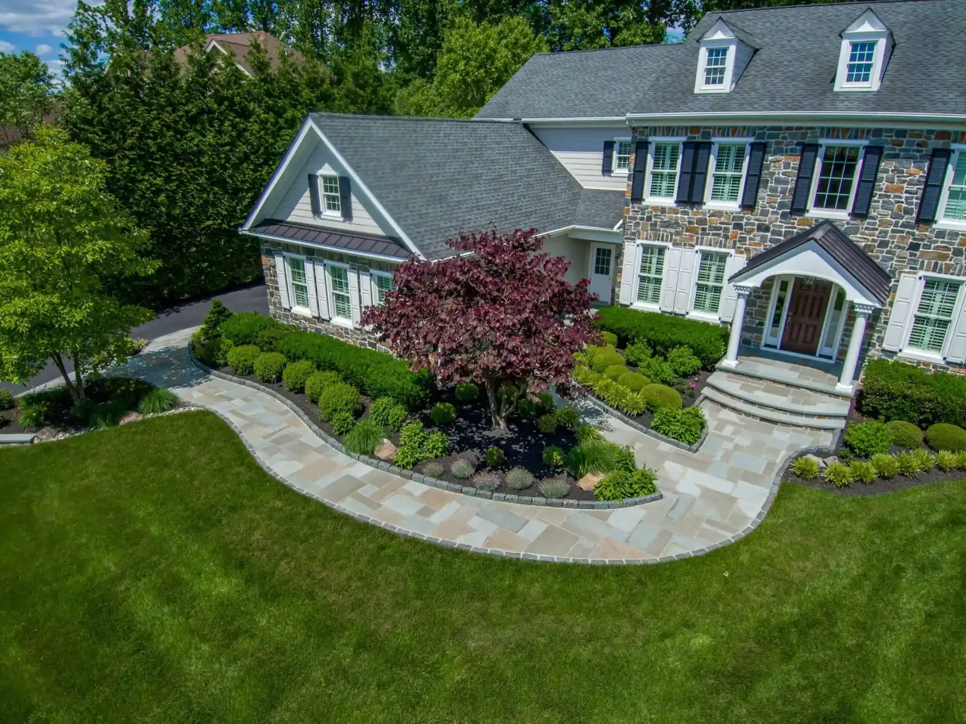 Large suburban house with a curved stone walkway, manicured lawn, and landscaped garden in front
