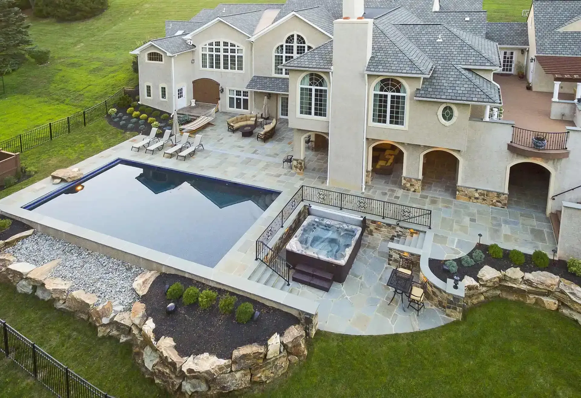 Aerial view of a large luxury house with a swimming pool, spa, and landscaped backyard.