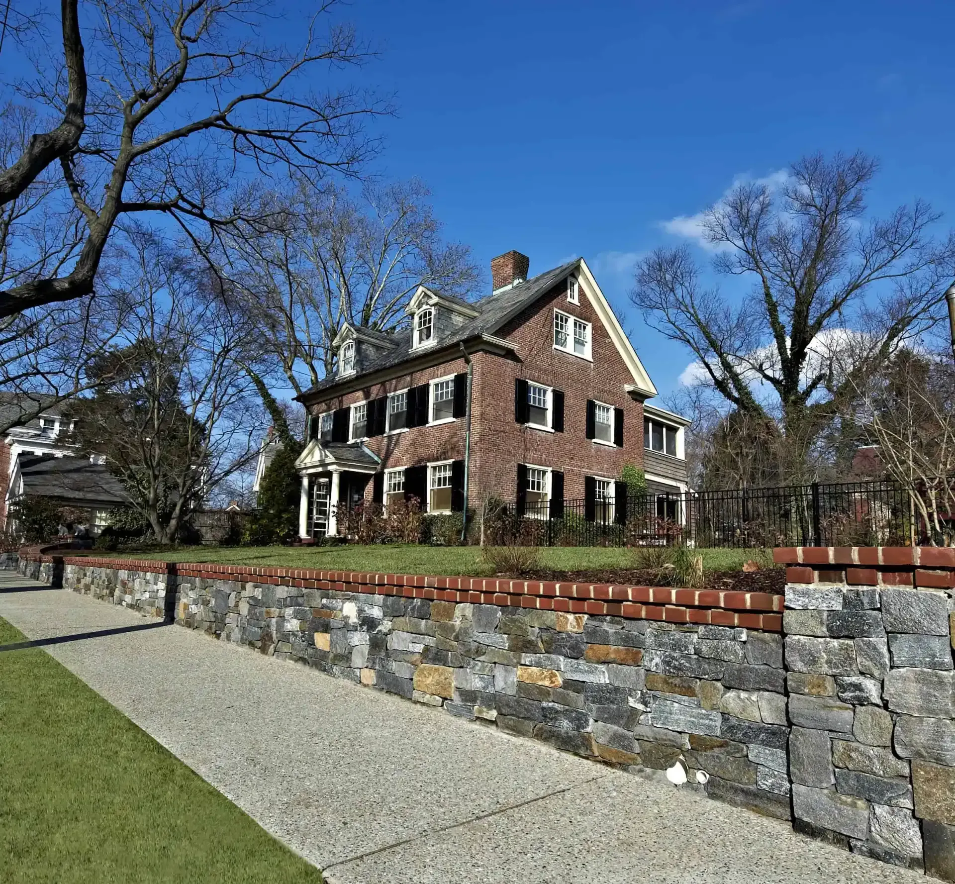Brick house with white trim behind a stone retaining wall and gravel path on a sunny day