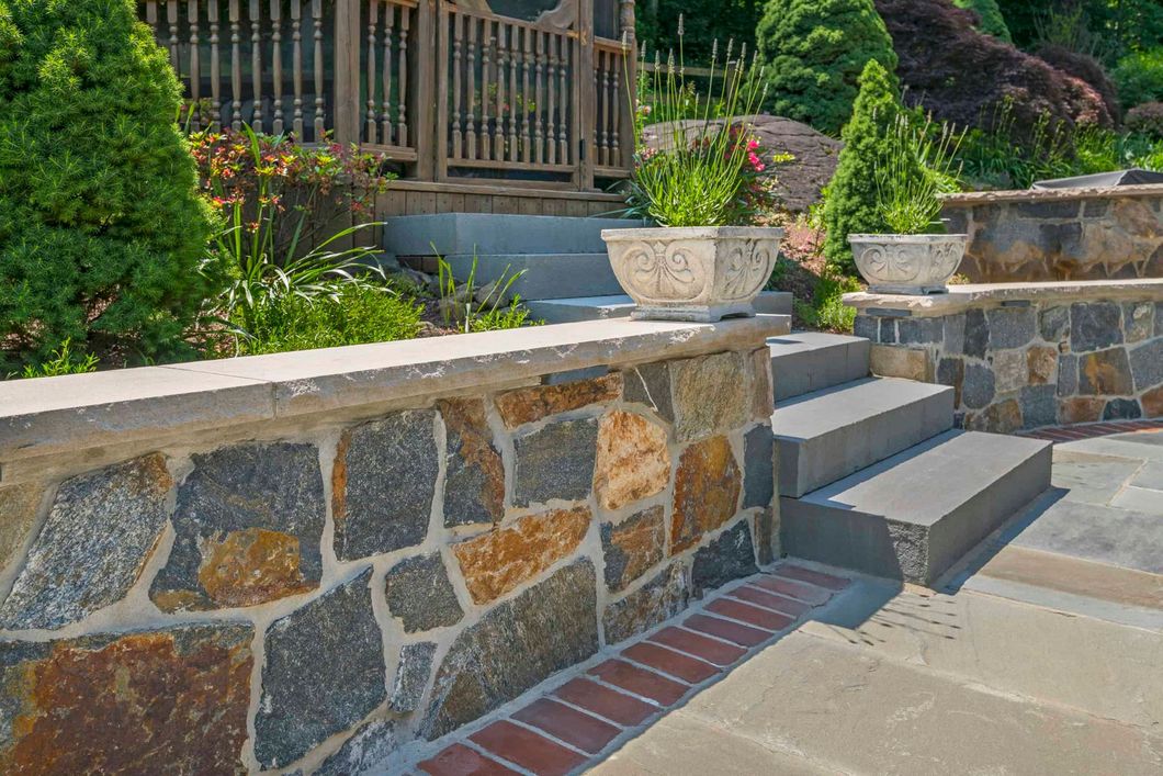 Stone retaining wall and steps beside a landscaped garden and patio.