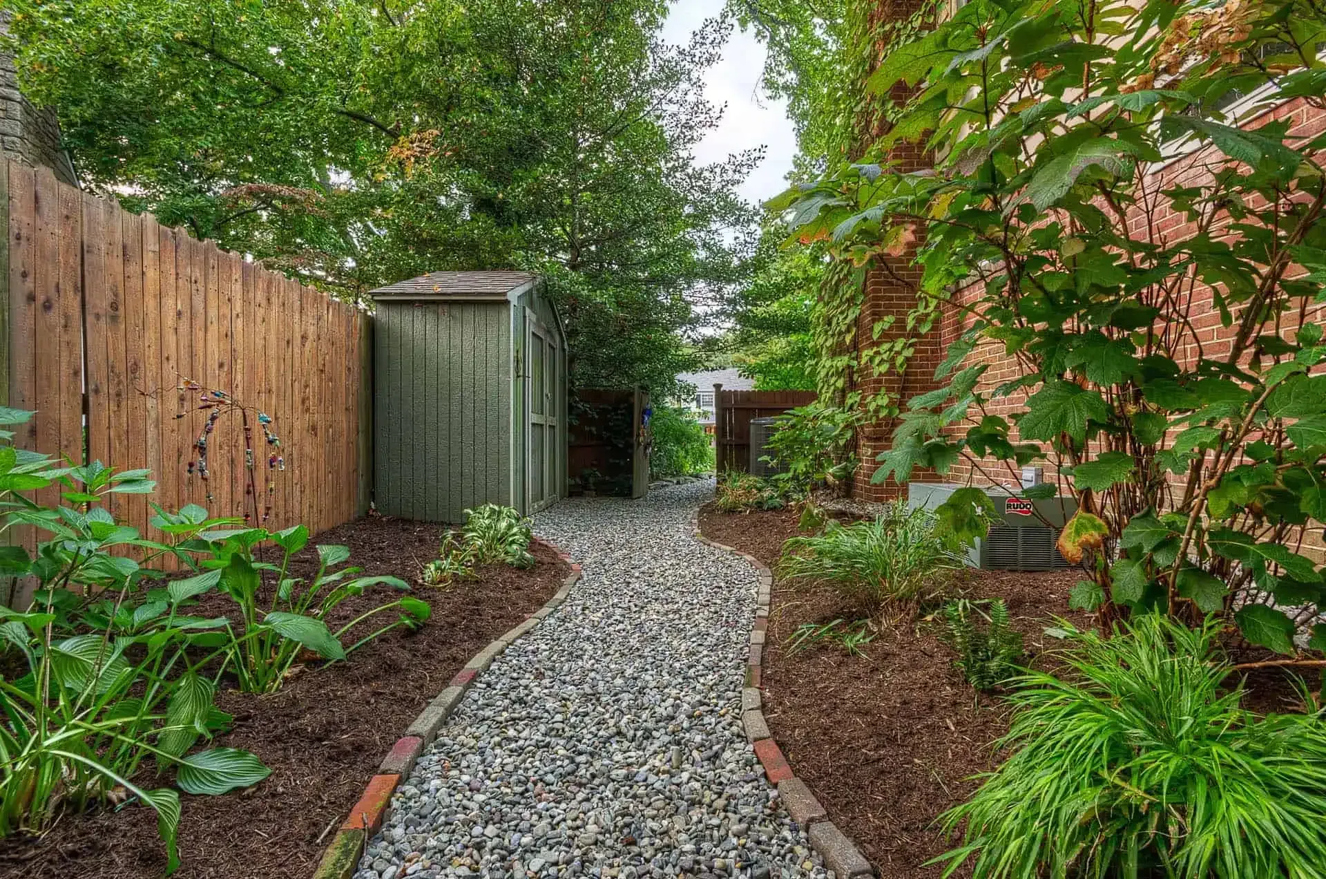 Gravel garden path between wooden fence and lush green plants, leading to a shed.