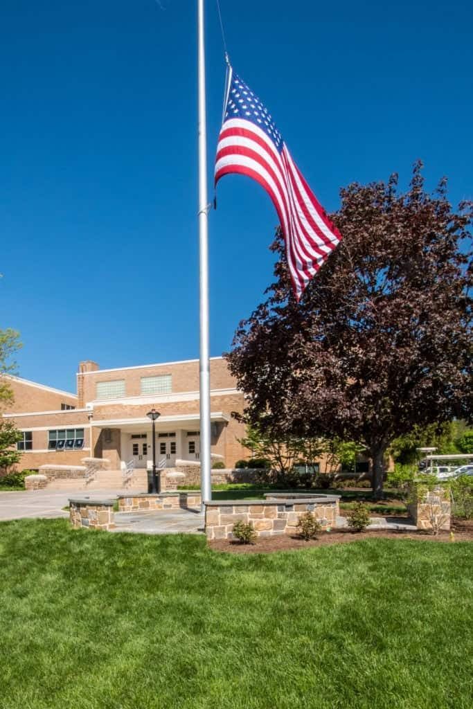 American flag flying in front of a brick building with a green lawn and blue sky